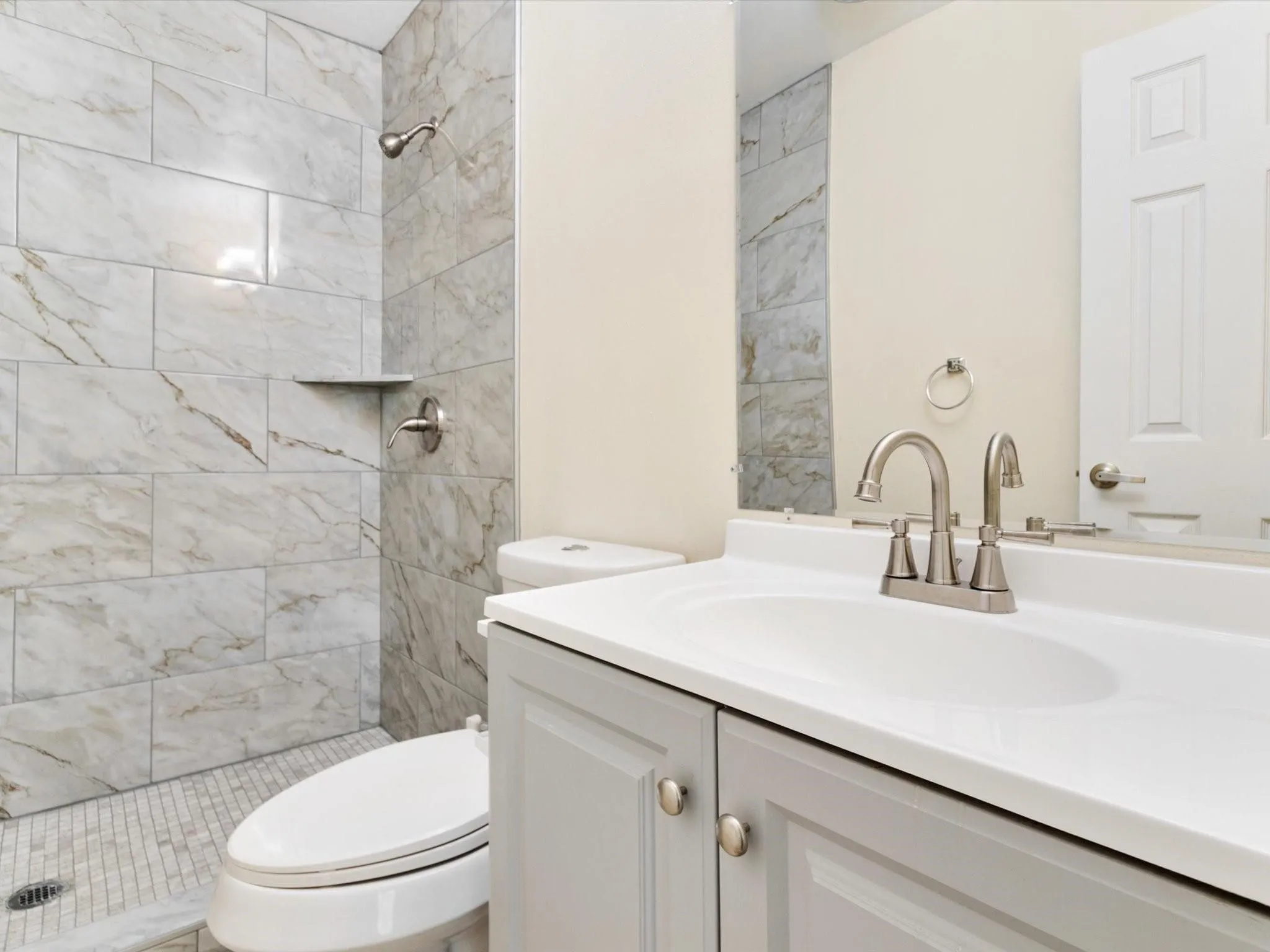 Shower with large format tile surround, tile shower floor, built-in shower niche, gray vanity with integrated sink, and brushed nickel hardware