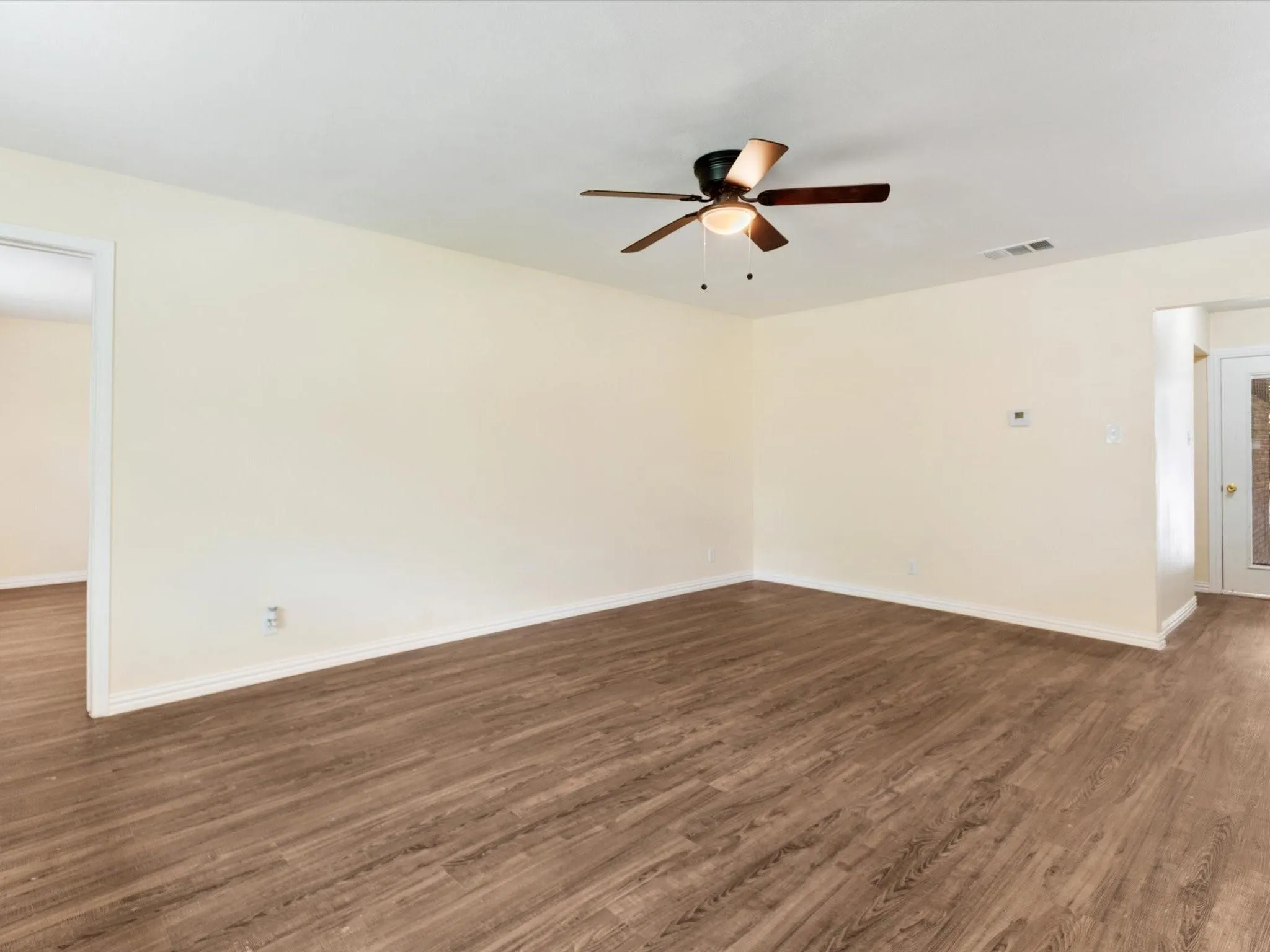 Wood-finish flooring throughout, complemented by light-toned walls and a ceiling fan with integrated lighting
