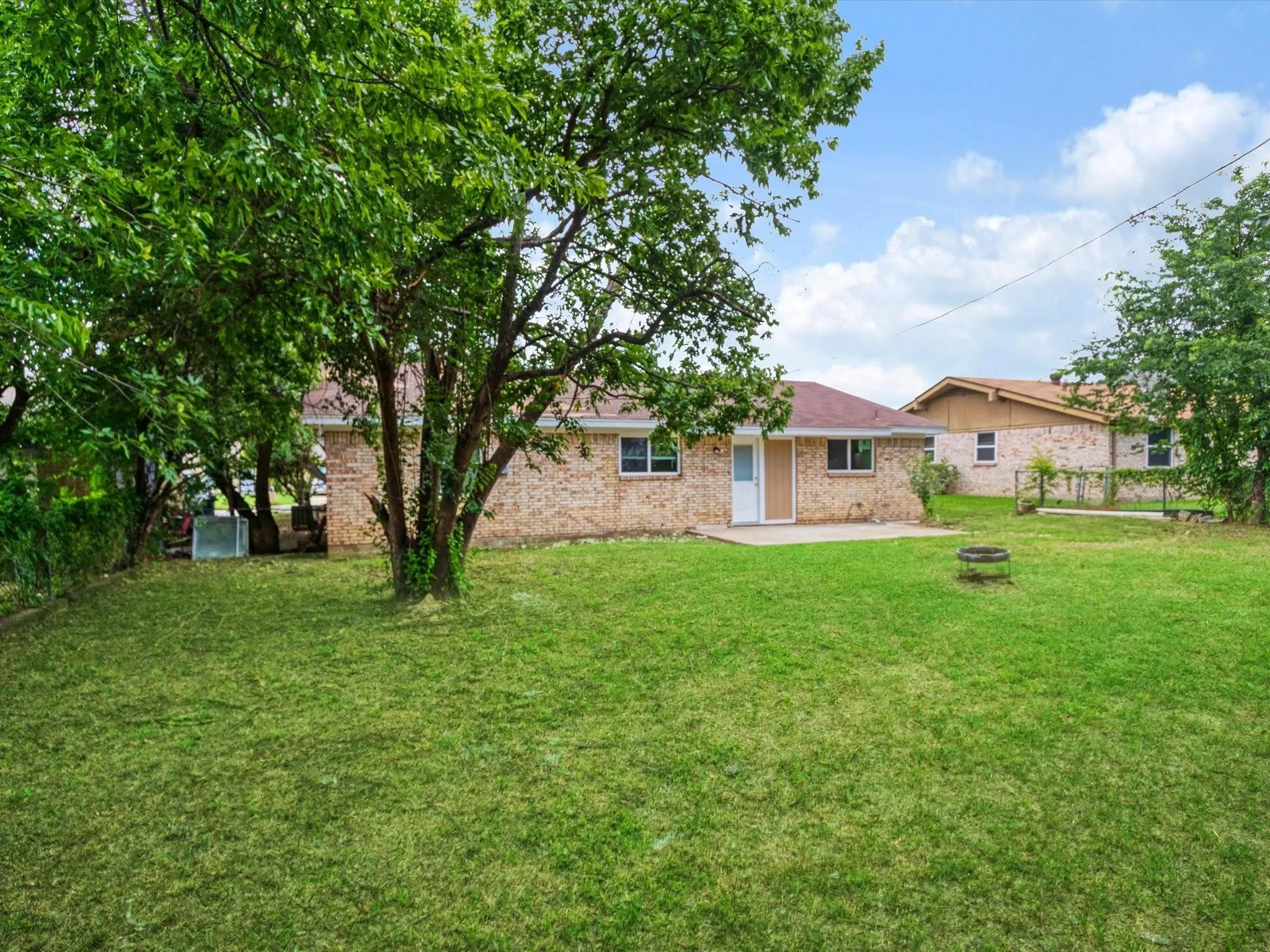 Expansive backyard featuring a manicured lawn, a large mature tree, a concrete patio, and a brick exterior
