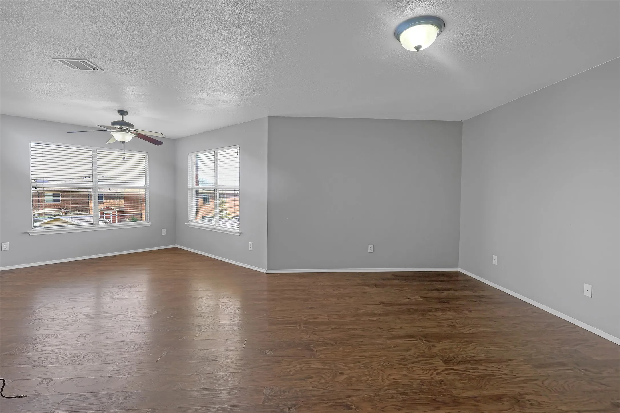 Empty room with a textured ceiling, ceiling fan, and dark wood-style floors