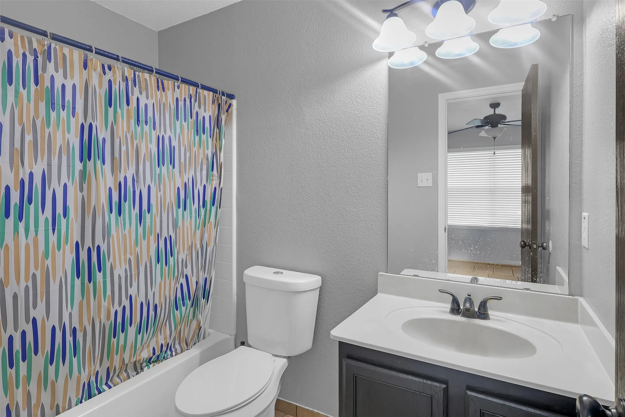 Full bathroom with a textured wall, shower / tub combo with curtain, vanity, and ceiling fan