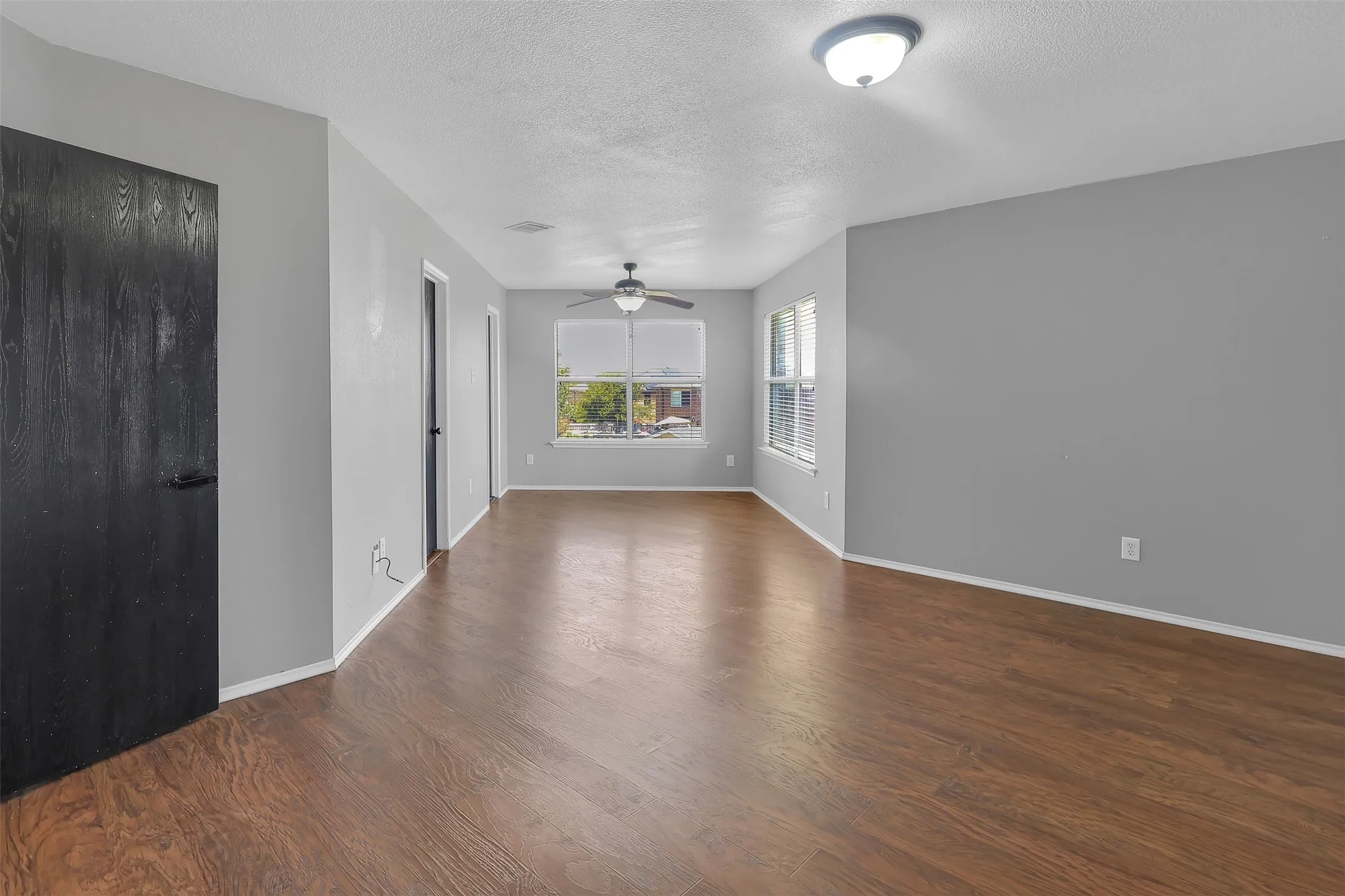 Unfurnished living room featuring a textured ceiling, dark wood-style flooring, and a ceiling fan