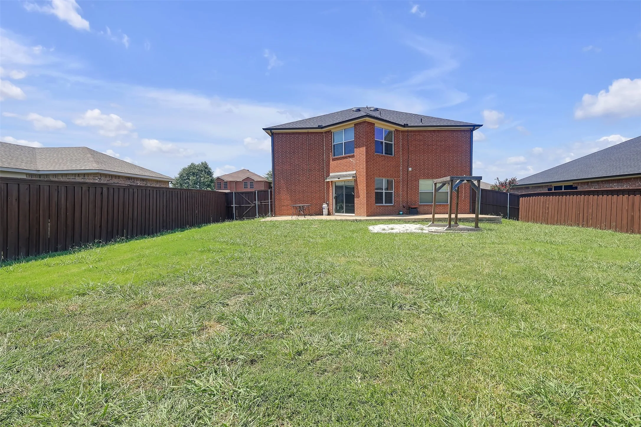 Rear view of property with brick siding, a fenced backyard, and a patio