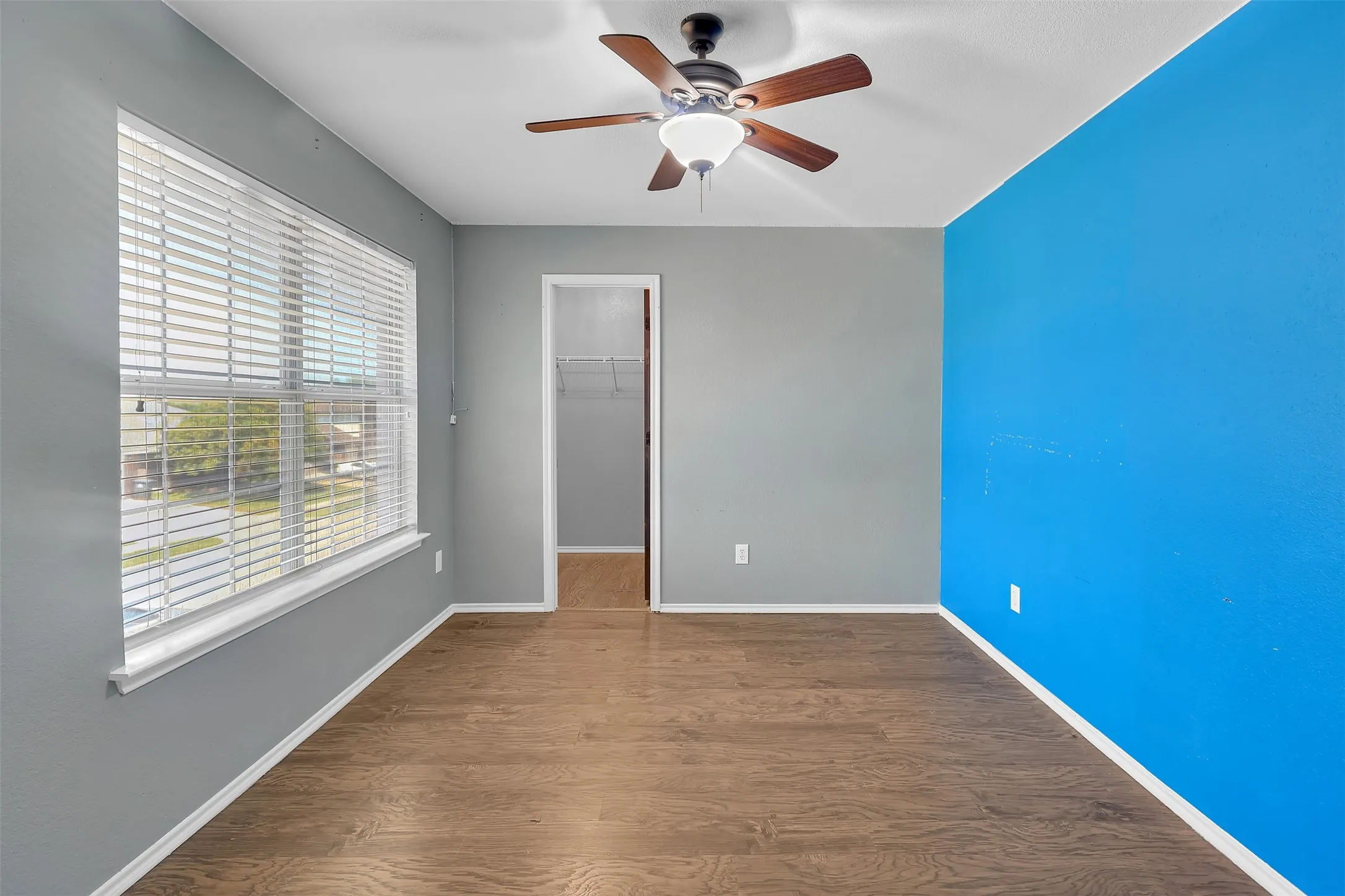 Unfurnished bedroom featuring dark wood-style floors, a spacious closet, and ceiling fan