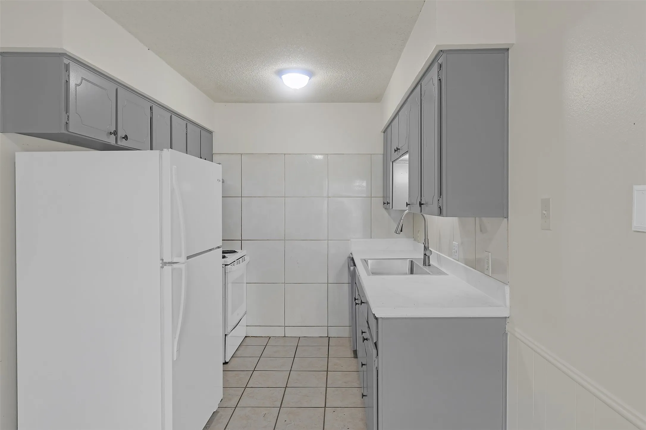 Kitchen with white appliances, gray cabinets, light tile patterned flooring, a textured ceiling, and light countertops