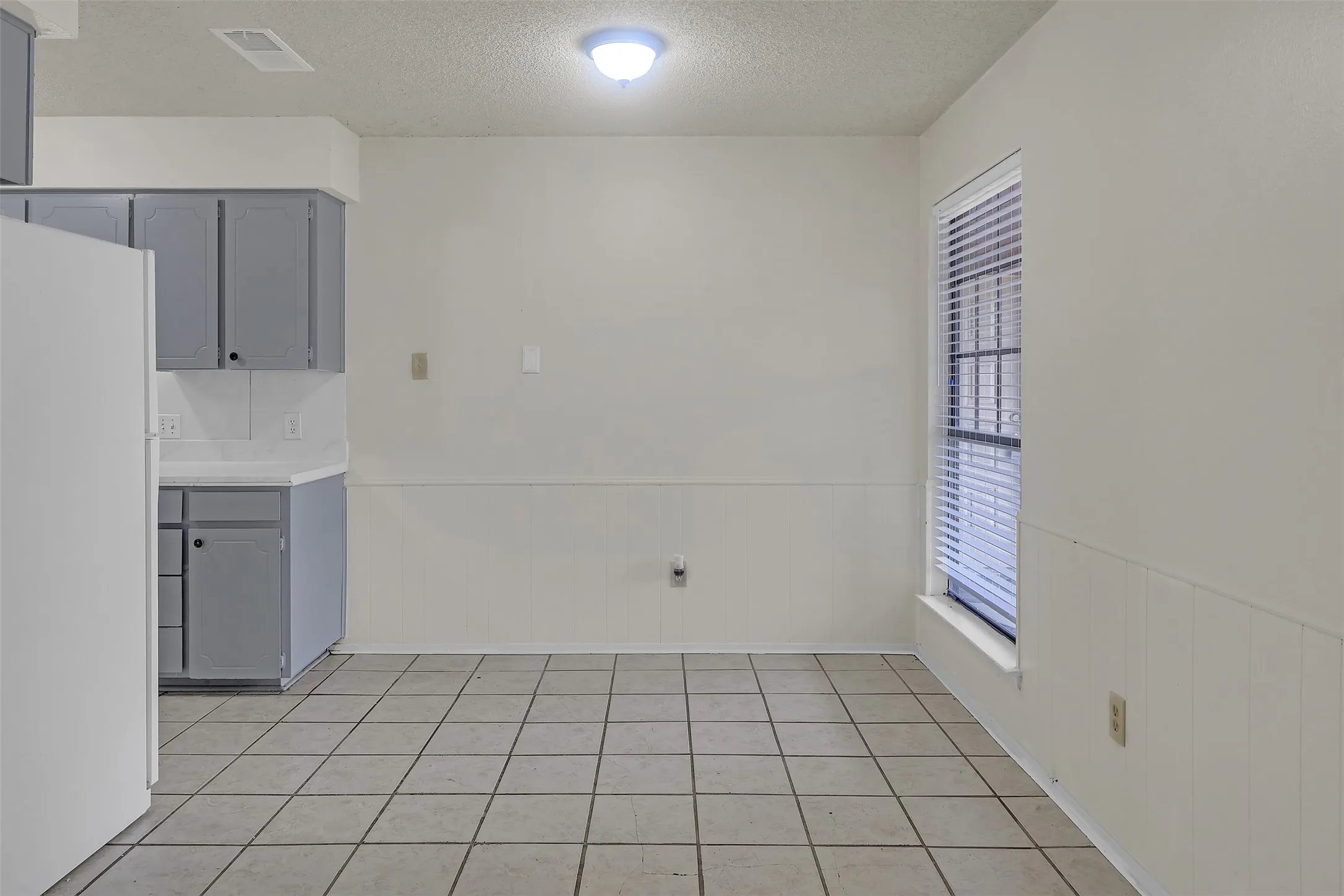 Unfurnished dining area featuring a textured ceiling and a wainscoted wall