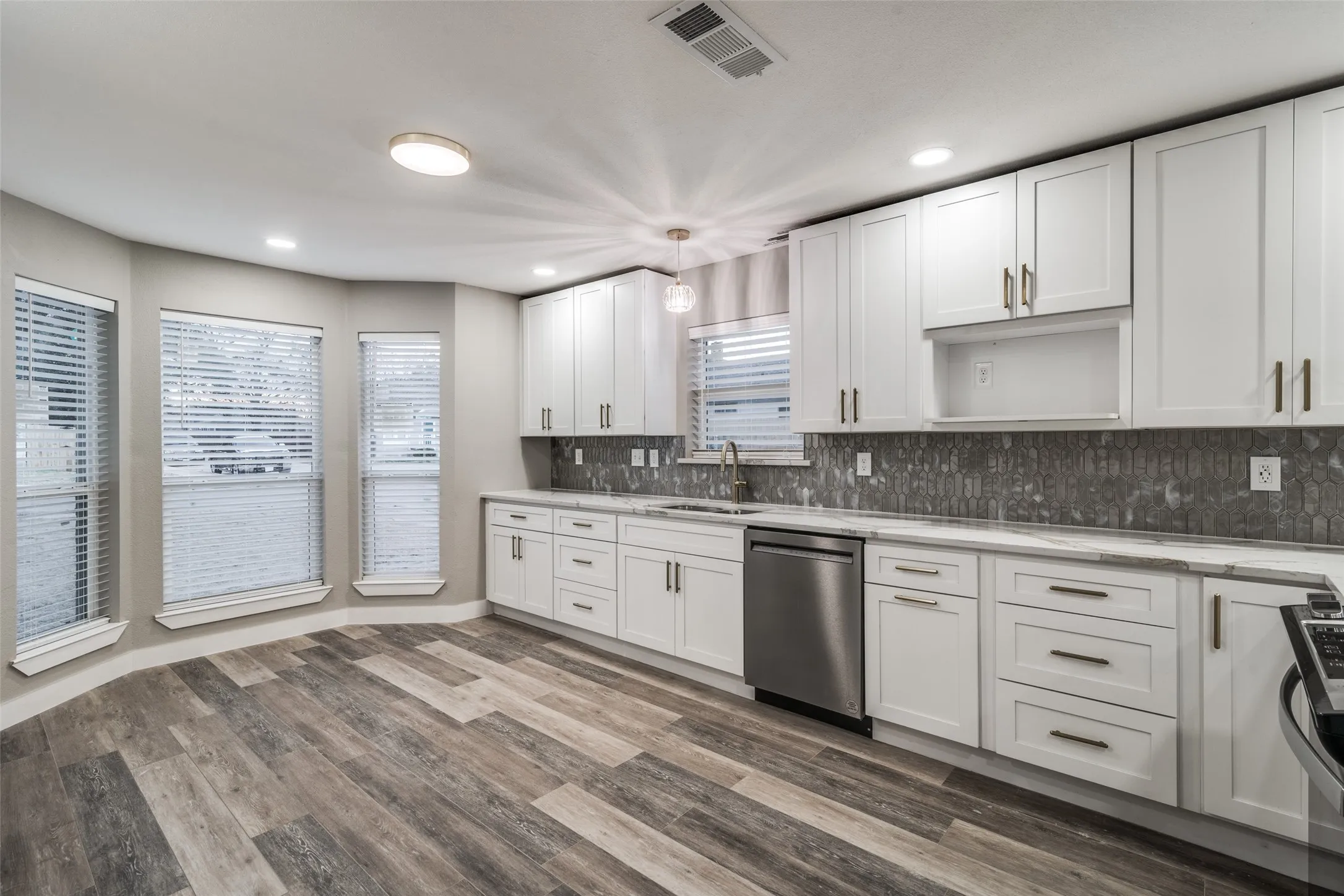 Kitchen featuring white cabinetry, gray hexagon tile backsplash, light stone countertops, stainless steel dishwasher, and wood-finish flooring