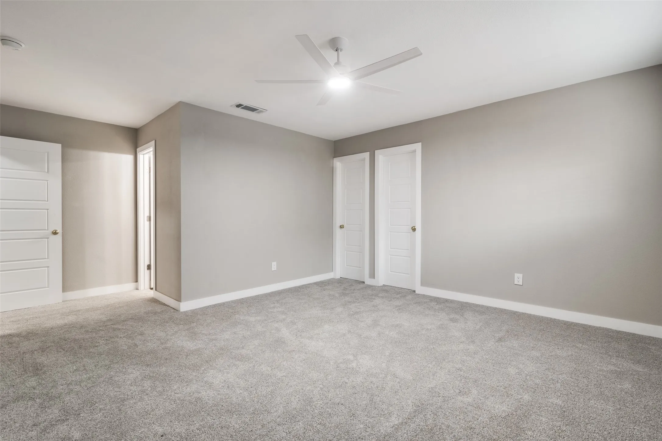 Spacious room featuring neutral grey walls, light grey carpet, white trim, and a ceiling fan with integrated lighting