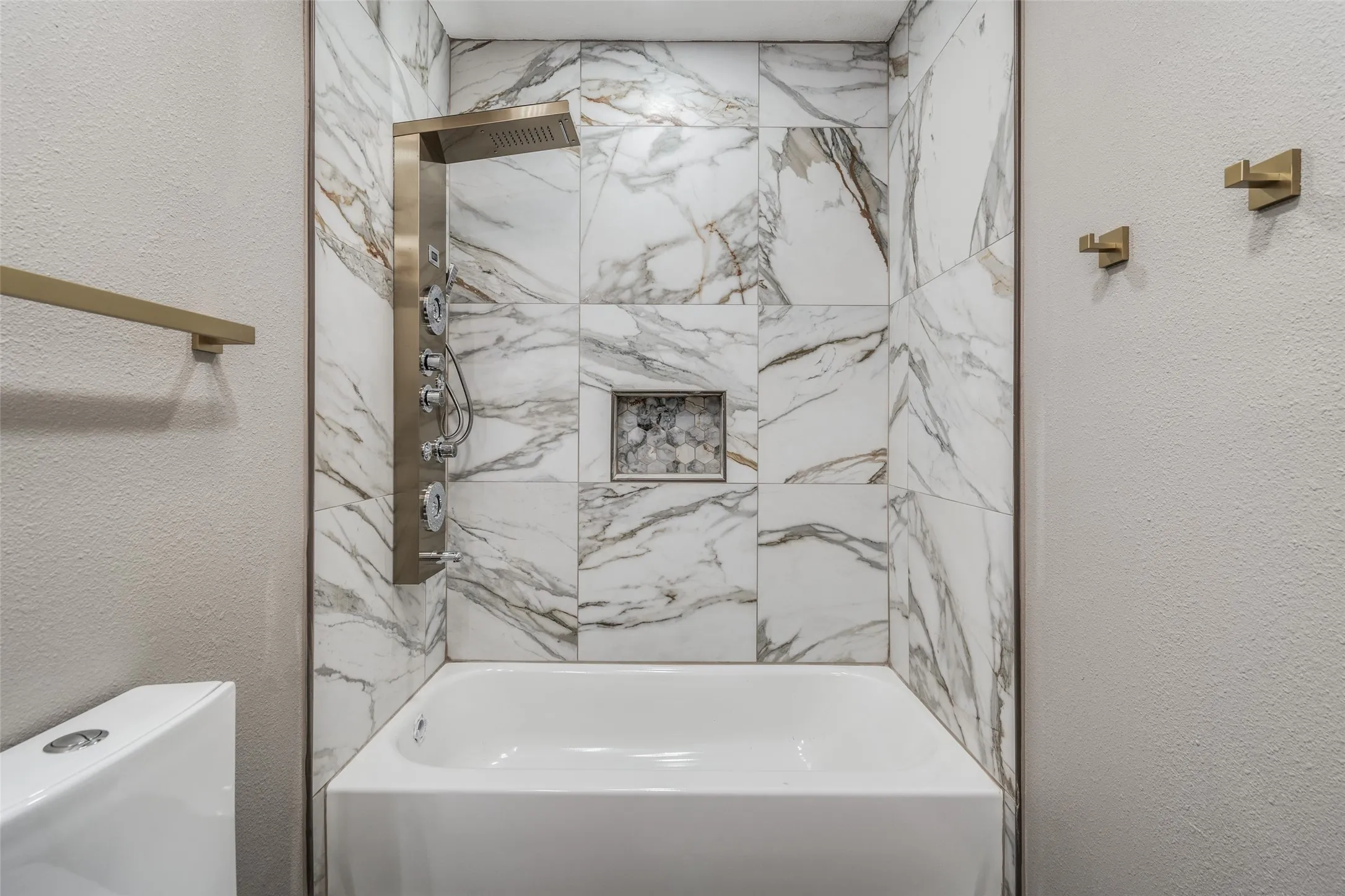 Bathtub with full-height patterned tile surround, stainless steel multi-function shower panel, and integrated shower niche