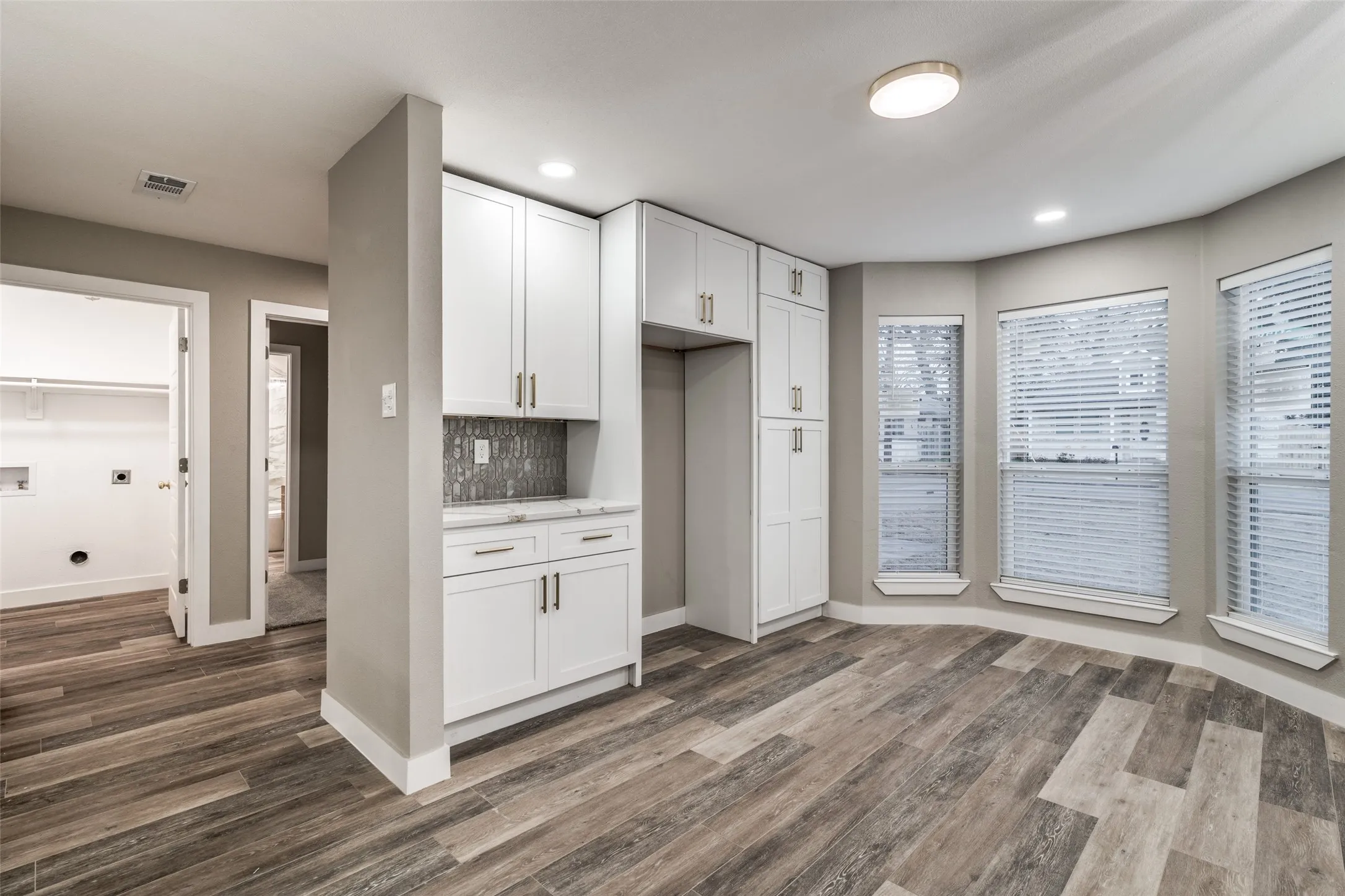White cabinetry, wood-finish flooring, bay windows, recessed lighting, and a tile backsplash