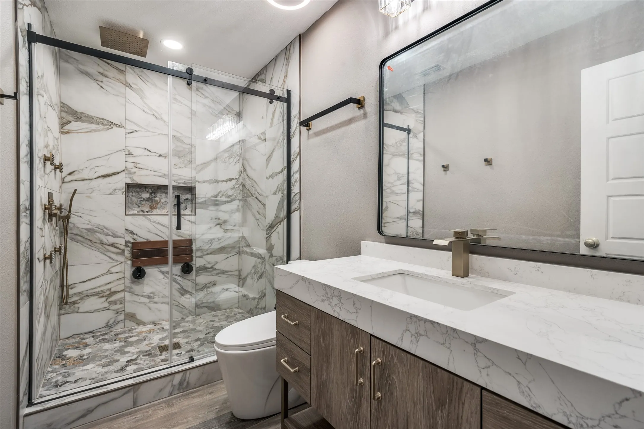 Marble-patterned shower with a sliding glass door, built-in shelving, and a mosaic tile floor