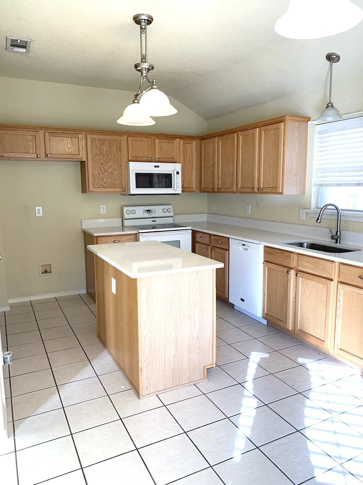 Kitchen featuring wood cabinetry, white appliances, a center island with a light-toned countertop, and tile flooring