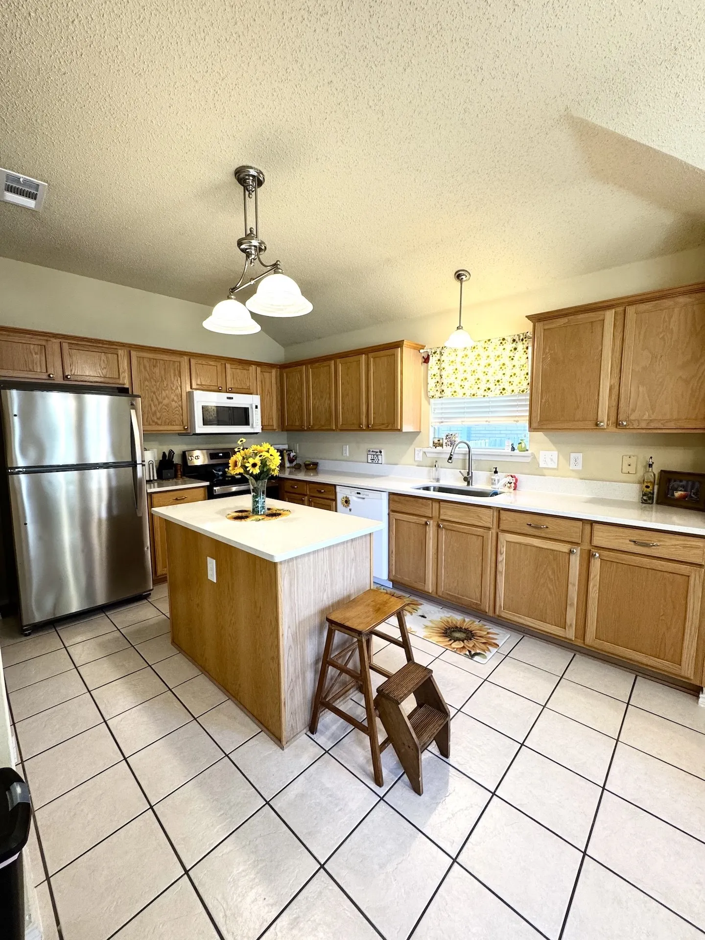Kitchen featuring wood cabinetry, stainless steel appliances, a center island with a light-toned countertop, and tile flooring