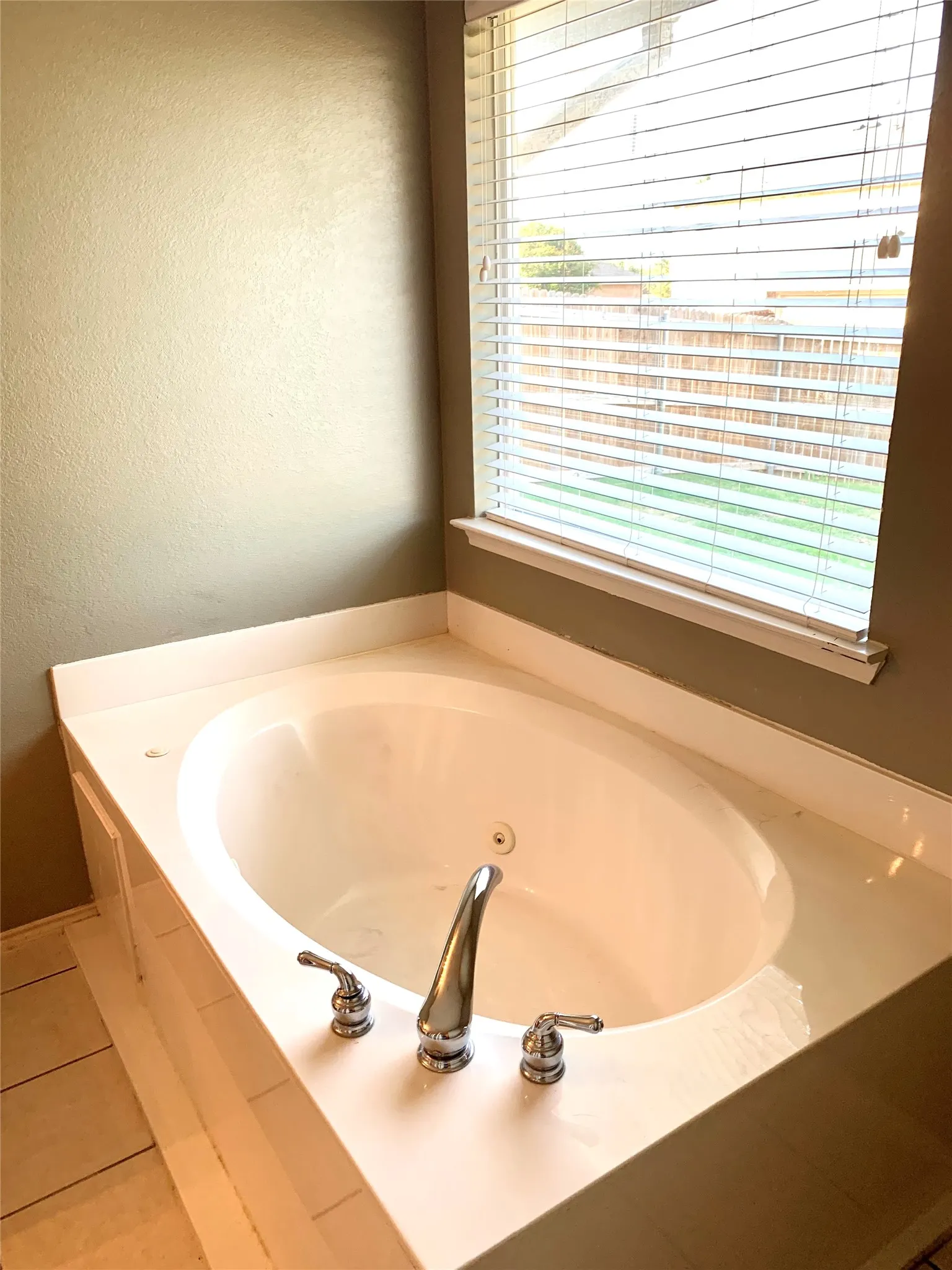 Alcove bathtub featuring a white surround, chrome fixtures, and a corner window with horizontal blinds