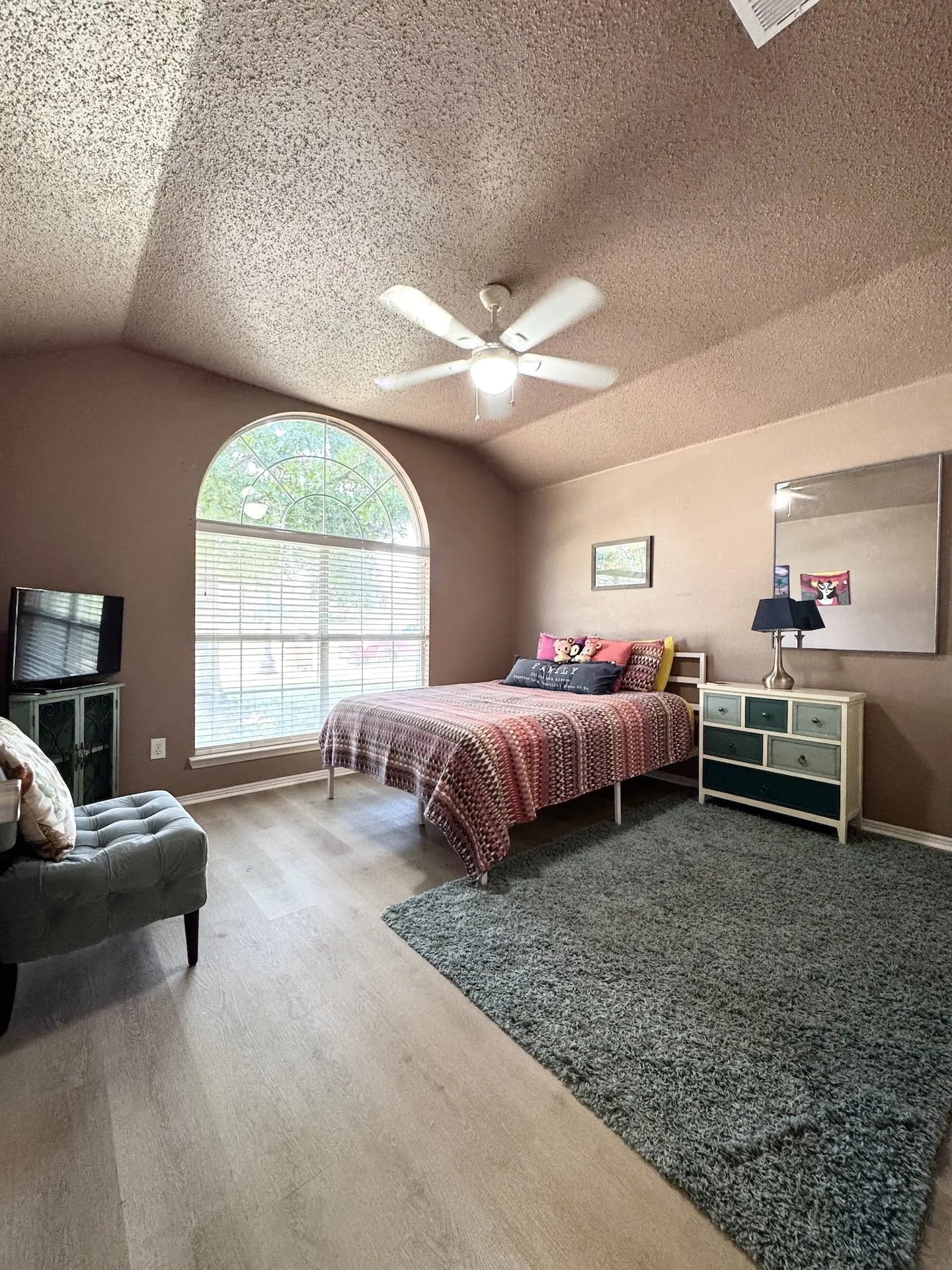Vaulted ceiling with a ceiling fan, arched window with horizontal blinds, light wood-finish flooring, and painted walls
