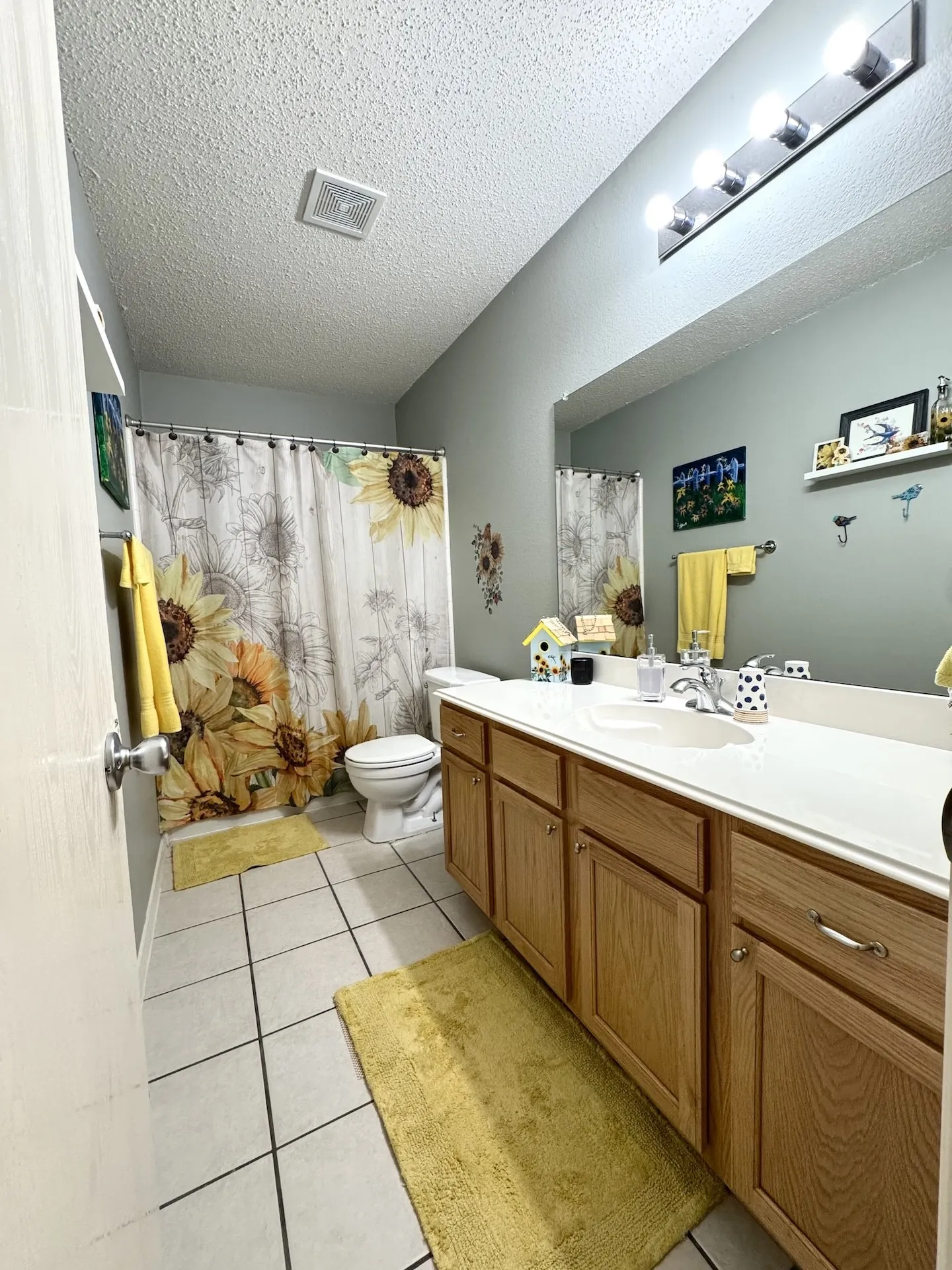 Bathroom featuring a wood-finish vanity with a white countertop and integrated sink, a large wall-mounted mirror, and tile flooring