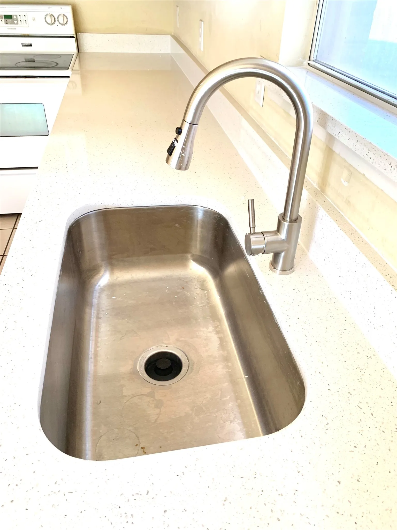 Stainless steel undermount sink, solid surface countertop, contemporary brushed nickel faucet, integrated spray nozzle, and white electric range