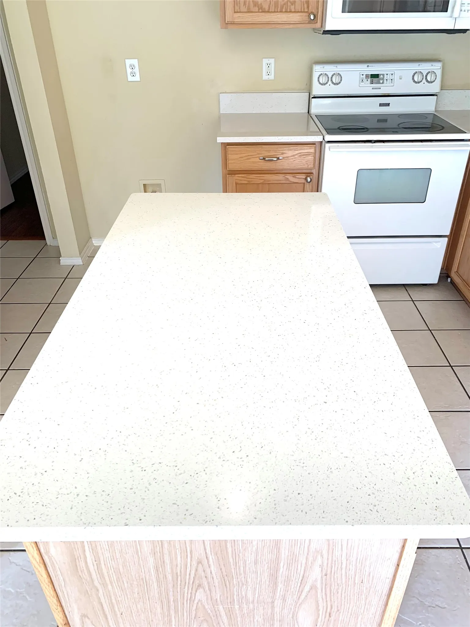 Kitchen island with a light-toned countertop, wood-finish base, tile flooring, and a white electric range