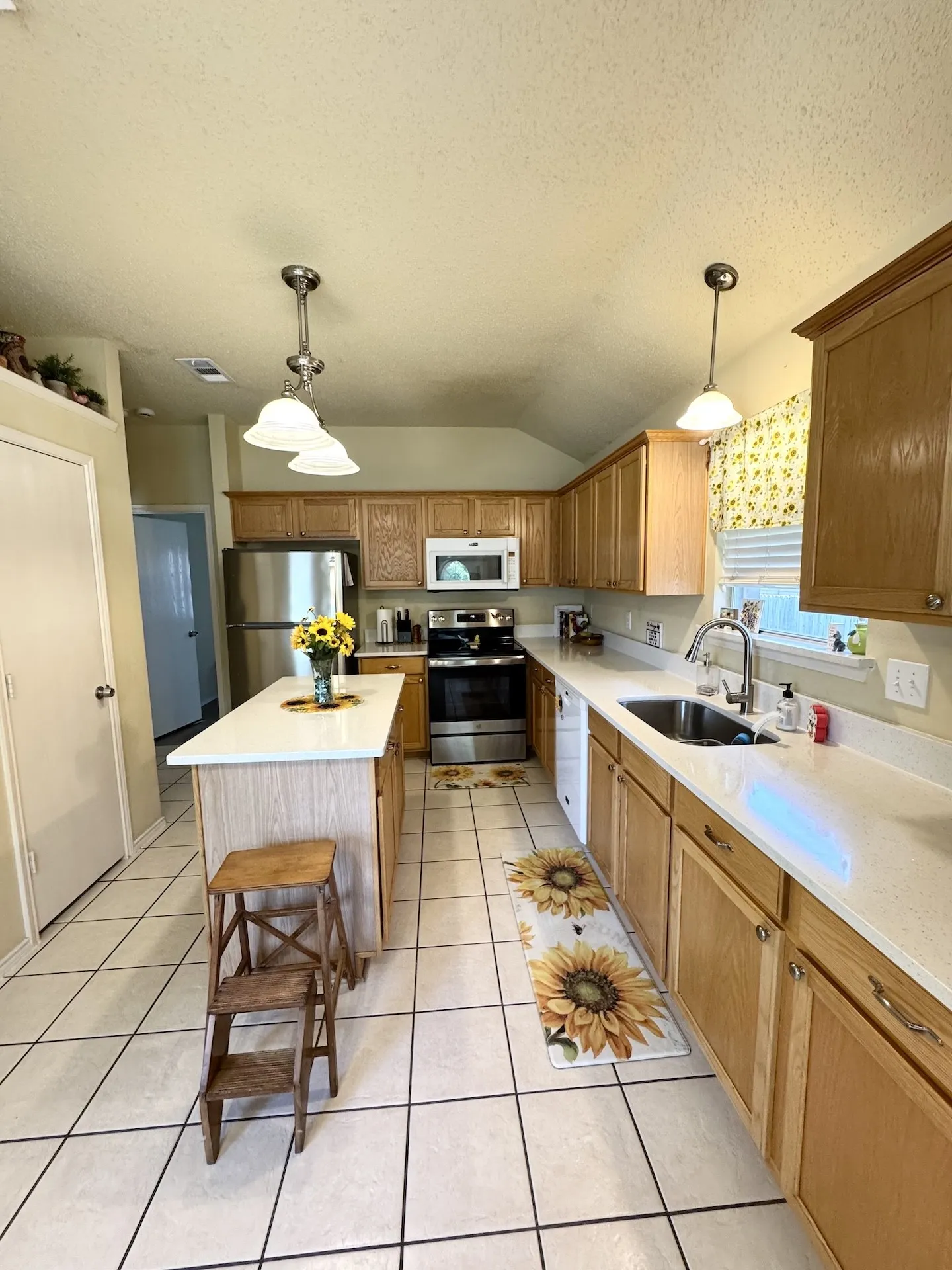 Kitchen featuring a central island with white countertop, extensive light wood cabinetry, stainless steel appliances, and white tile flooring