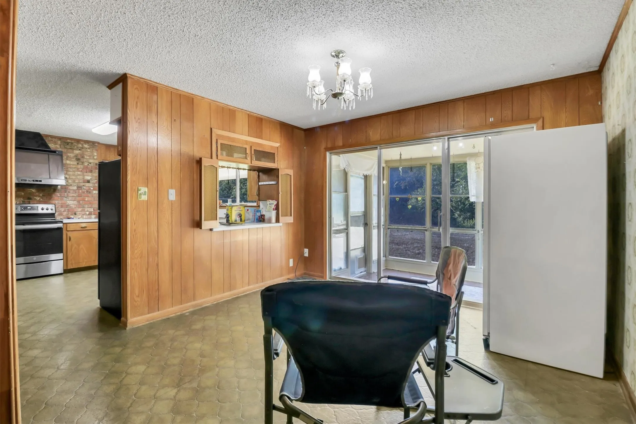 Wood paneling, built-in kitchen pass-through with cabinetry, chandelier lighting, and sliding glass doors