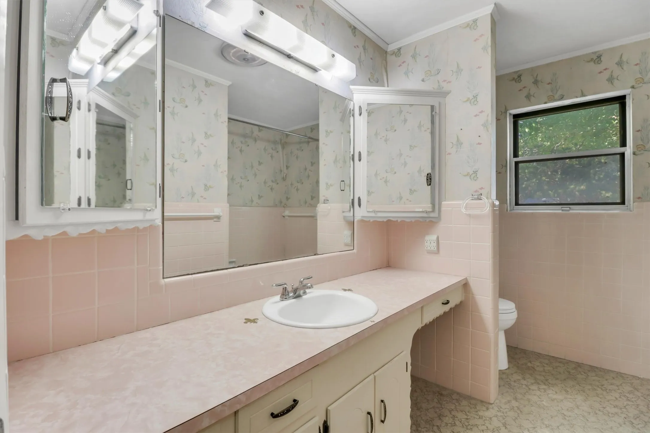 Vanity with integrated sink, expansive mirrored wall, built-in medicine cabinet, tiled wainscoting, and large window