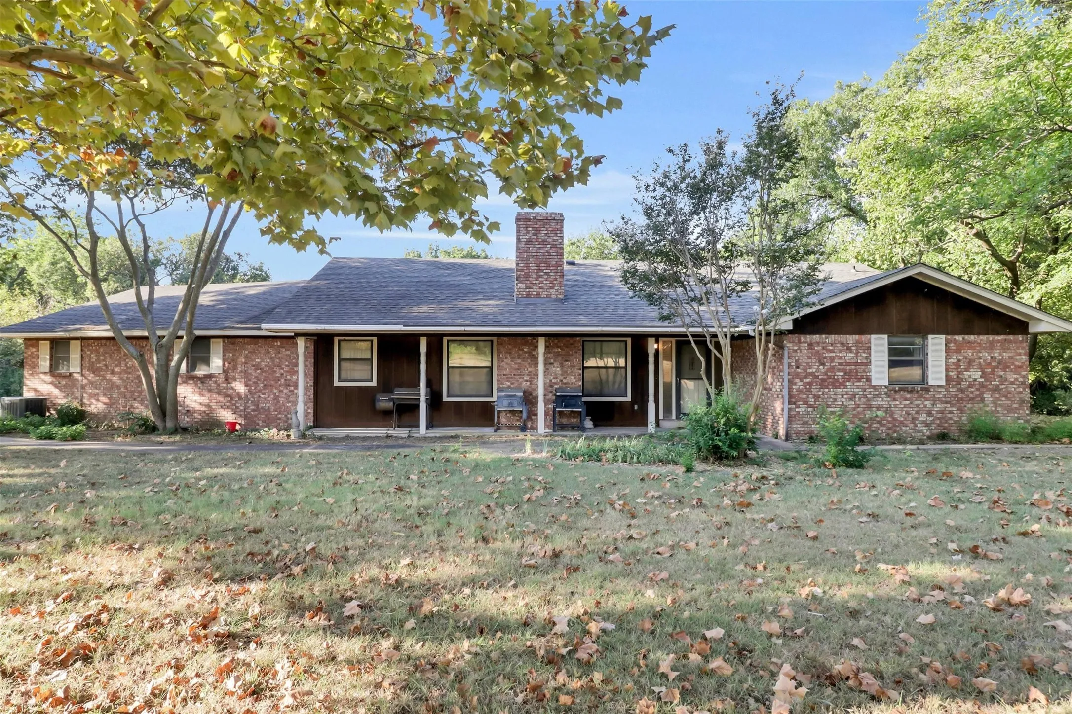 Brick exterior with a prominent brick chimney, covered front porch, and mature trees