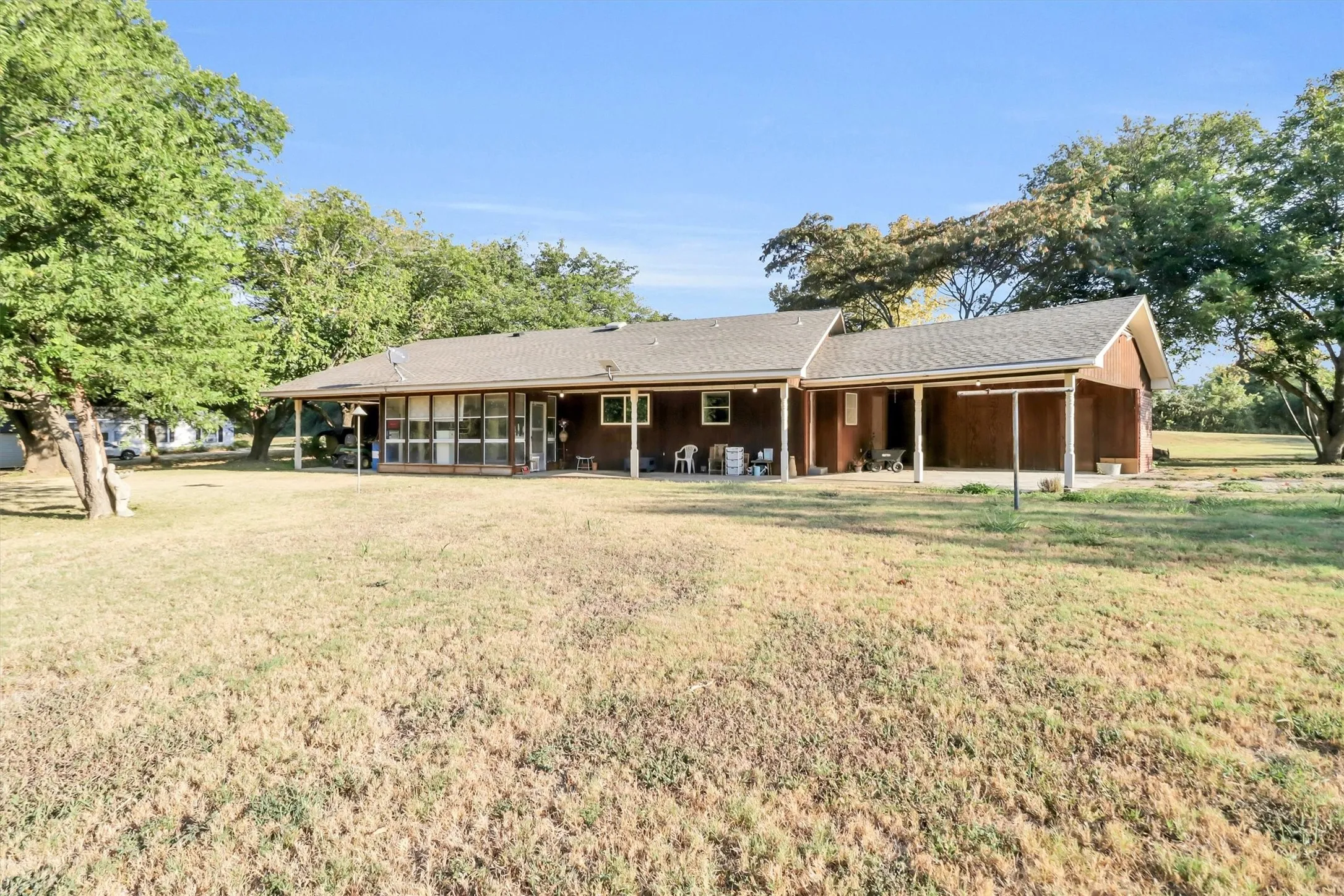 Expansive outdoor area with a covered patio, mature trees, and a gabled roofline