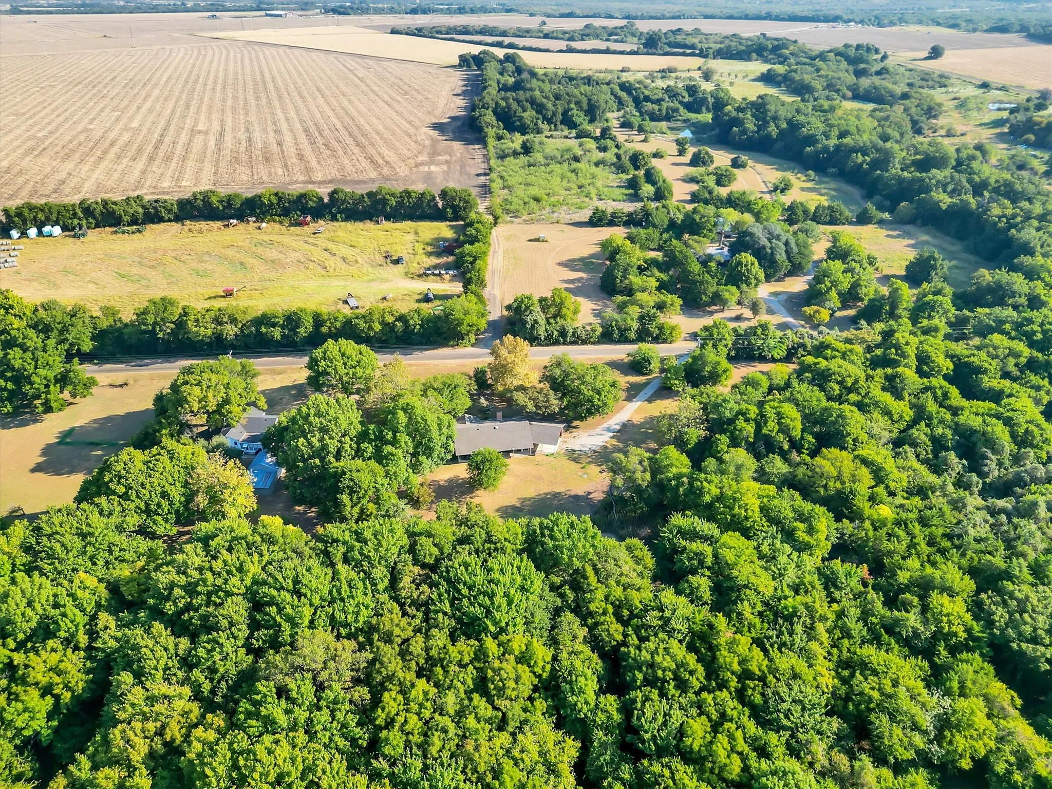 Expansive rural setting with a single-story residence, surrounded by mature trees, and bordered by agricultural fields