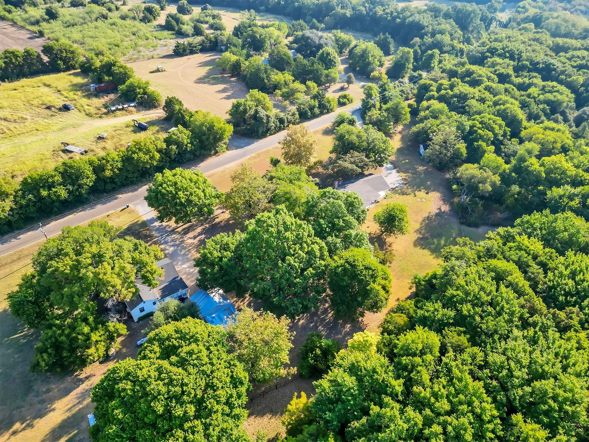 Expansive property featuring dense tree coverage, open grassy areas, and a paved road
