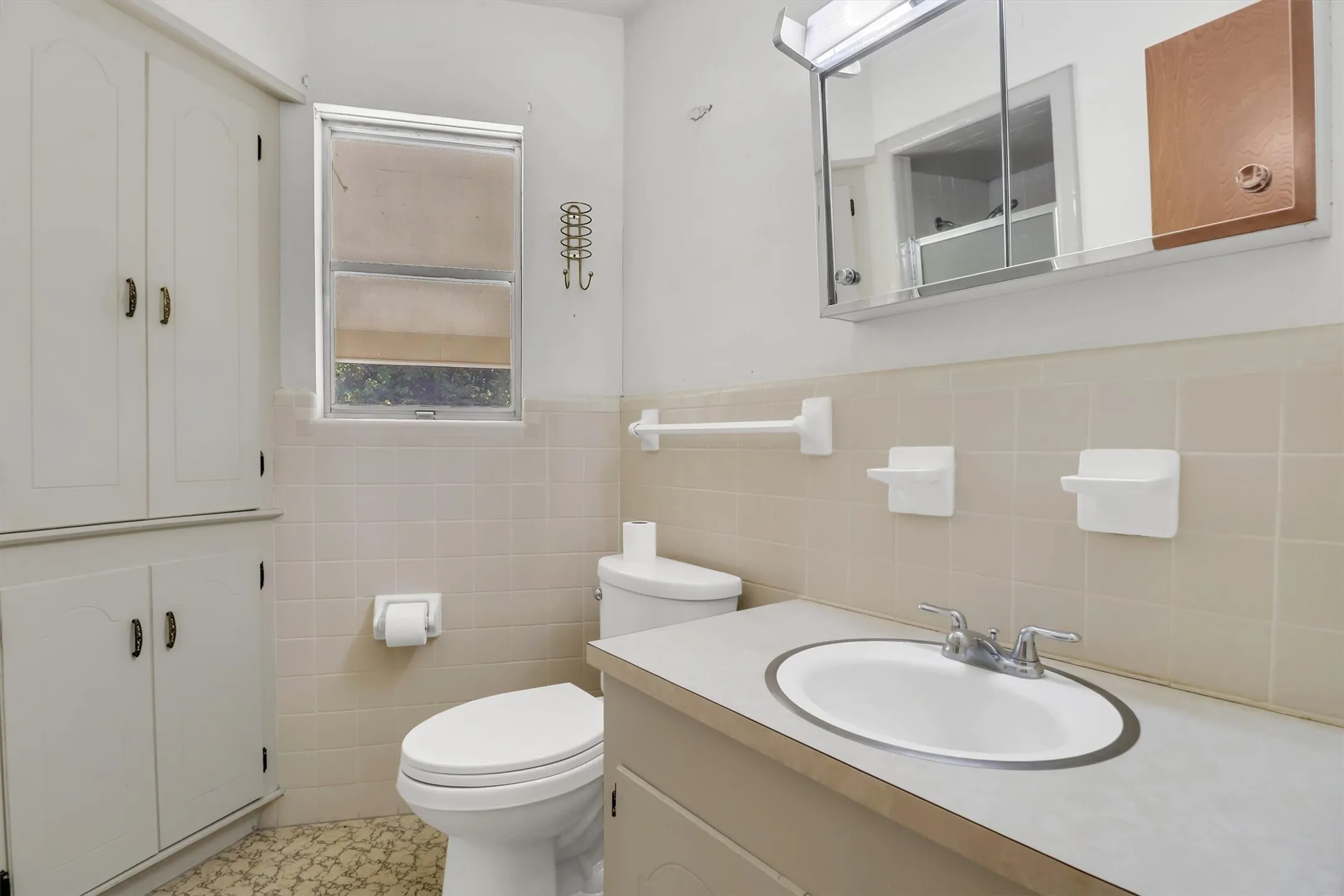 White built-in cabinetry, an integrated vanity sink, a wall-mounted mirror, and beige tiled walls