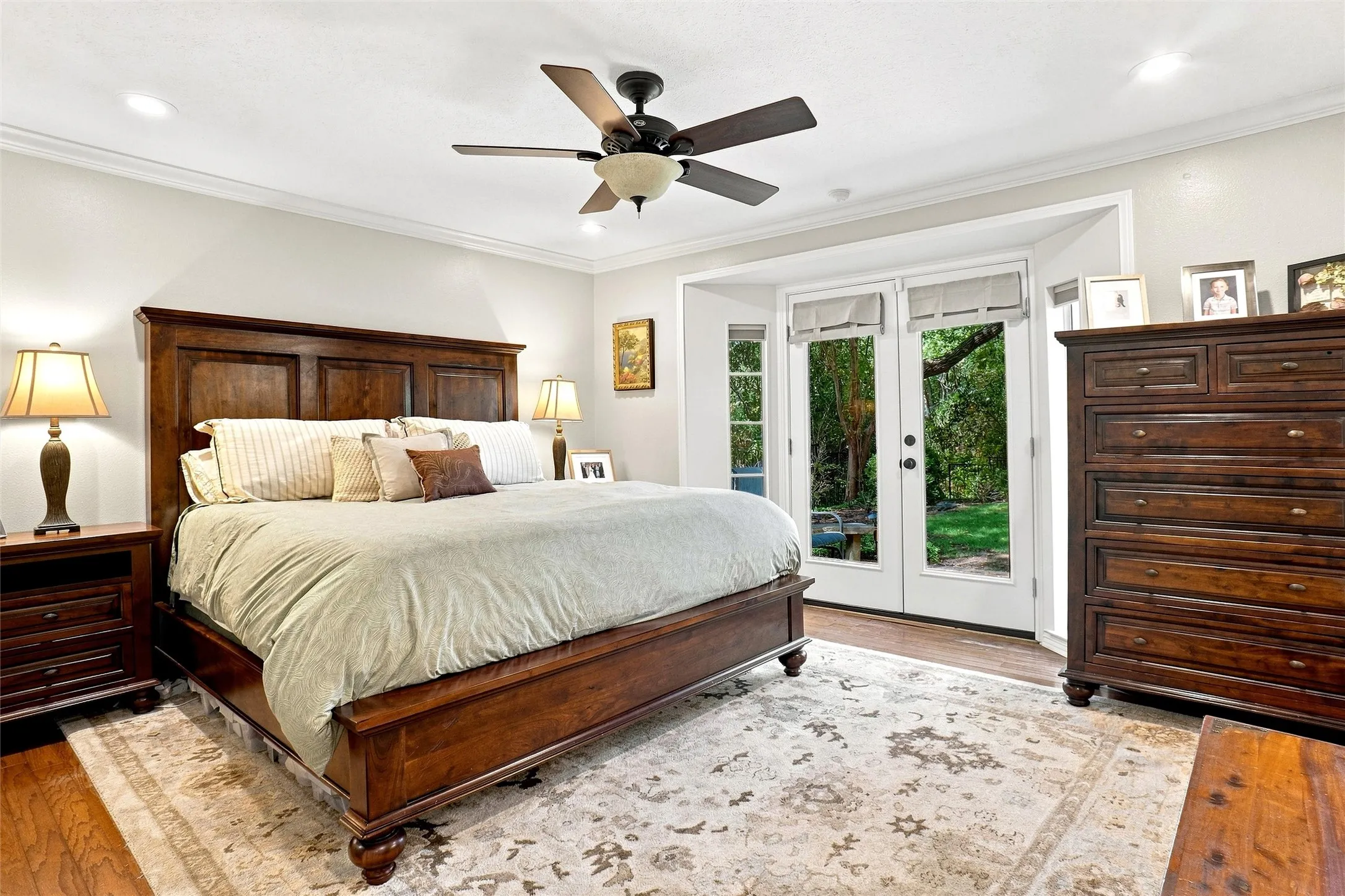 The downstairs primary suite features a large bayed area with double doors  flanked by side windows that are overlooking the grounds.  Here is crown molding, LED lighting, wood floors and a ceiling fan.  A beautiful relaxing room!