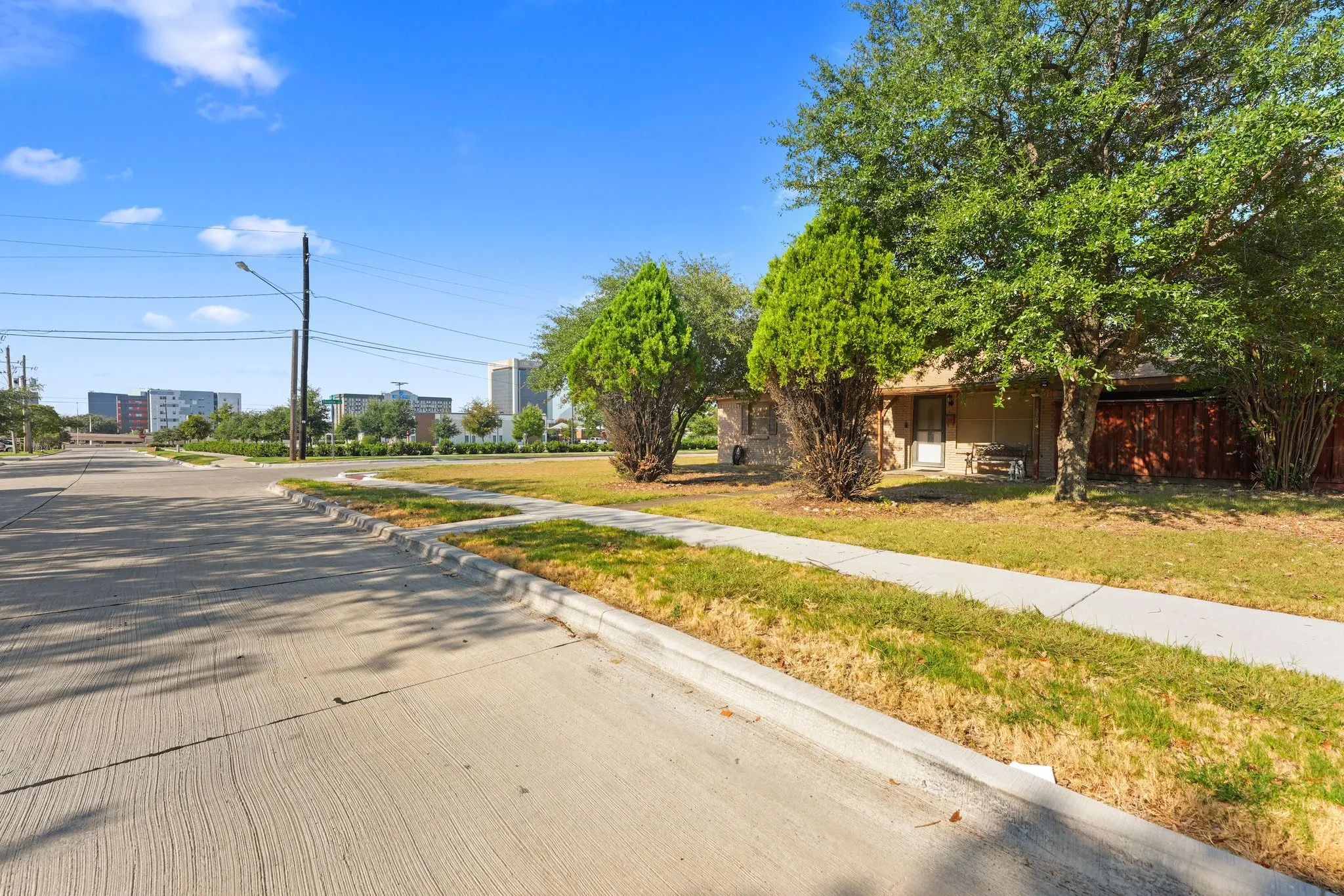 Single-story residence with a light-colored exterior, mature trees, and a wooden privacy fence