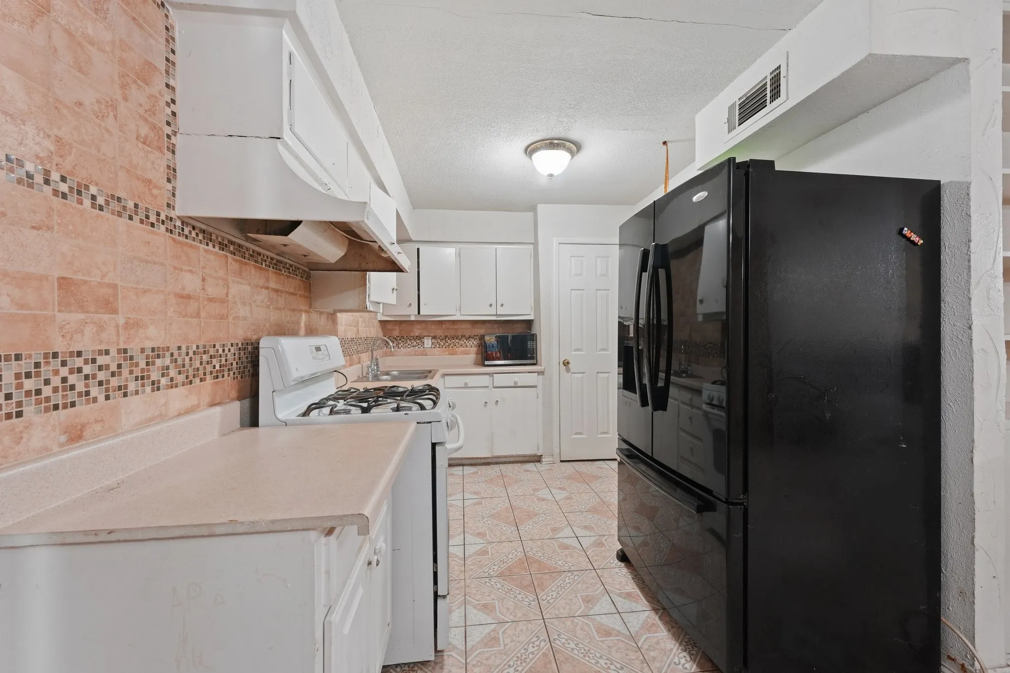 Kitchen featuring tile flooring, subway tile backsplash with mosaic accent, white cabinetry, and white countertops