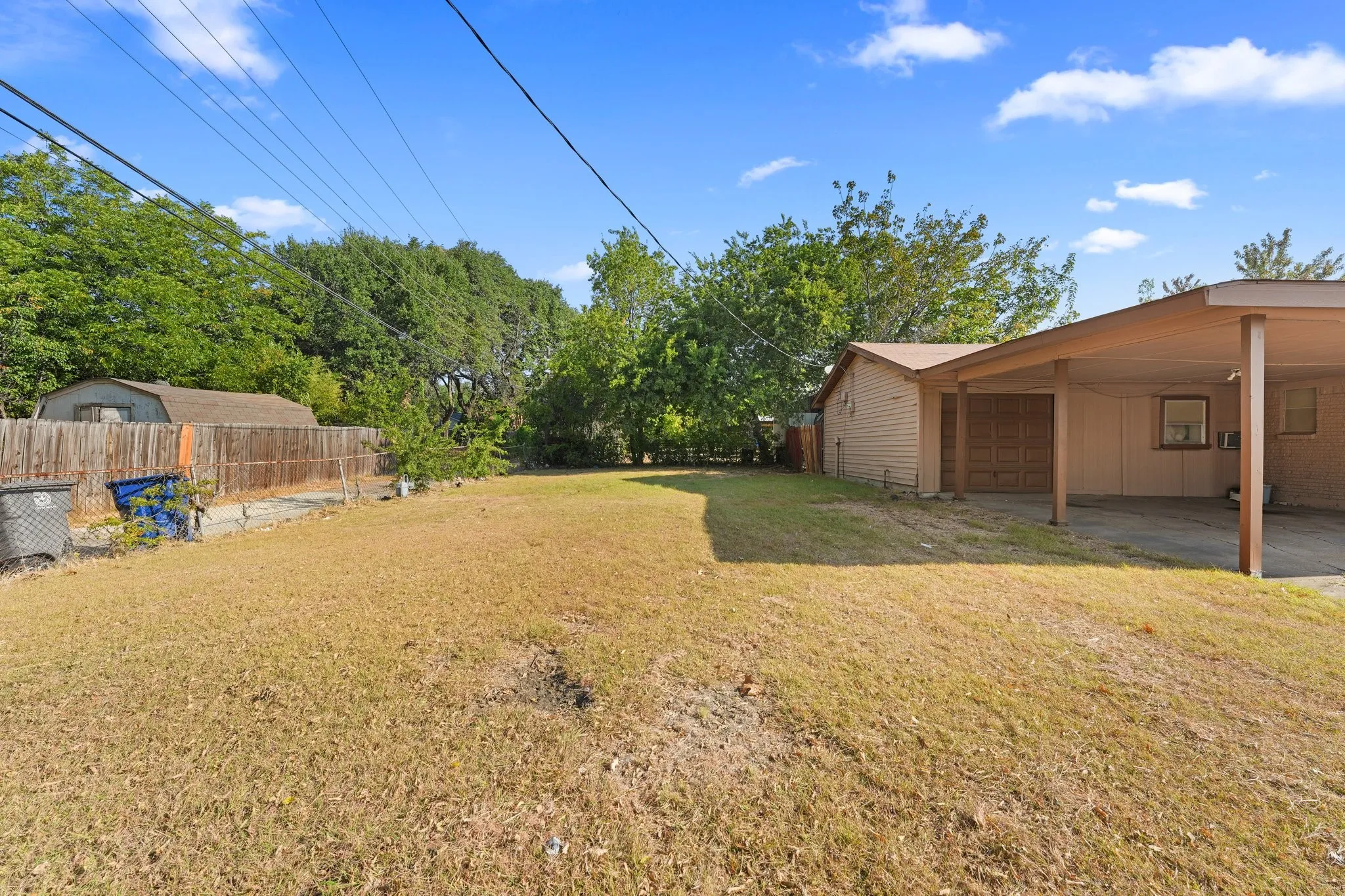 Expansive yard featuring a wooden privacy fence, mature trees, and a detached storage shed