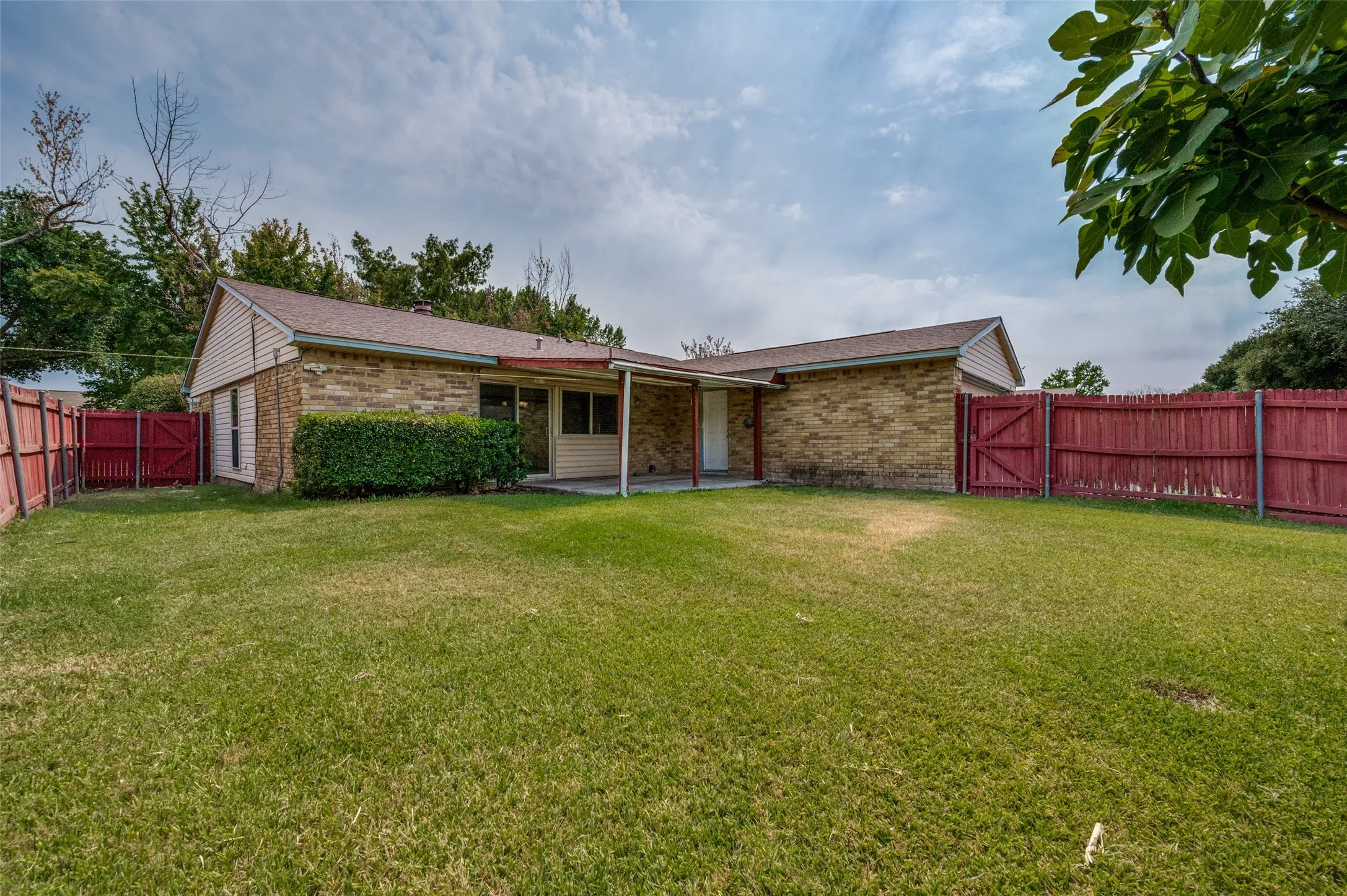 Expansive green lawn, red wood fencing, brick exterior, covered patio, and mature landscaping