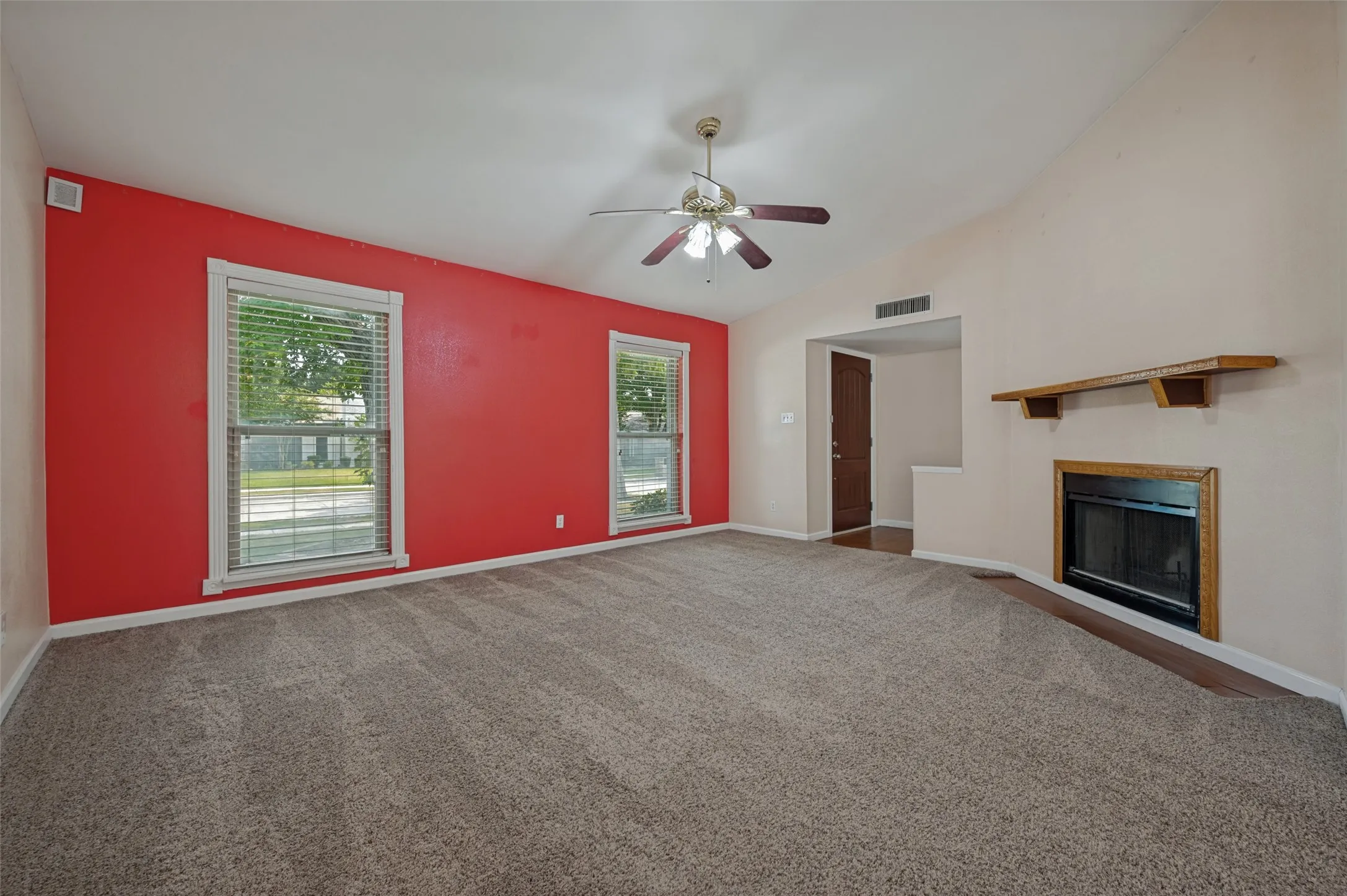 Vaulted ceiling with ceiling fan, two windows with blinds, built-in fireplace, and wood mantel
