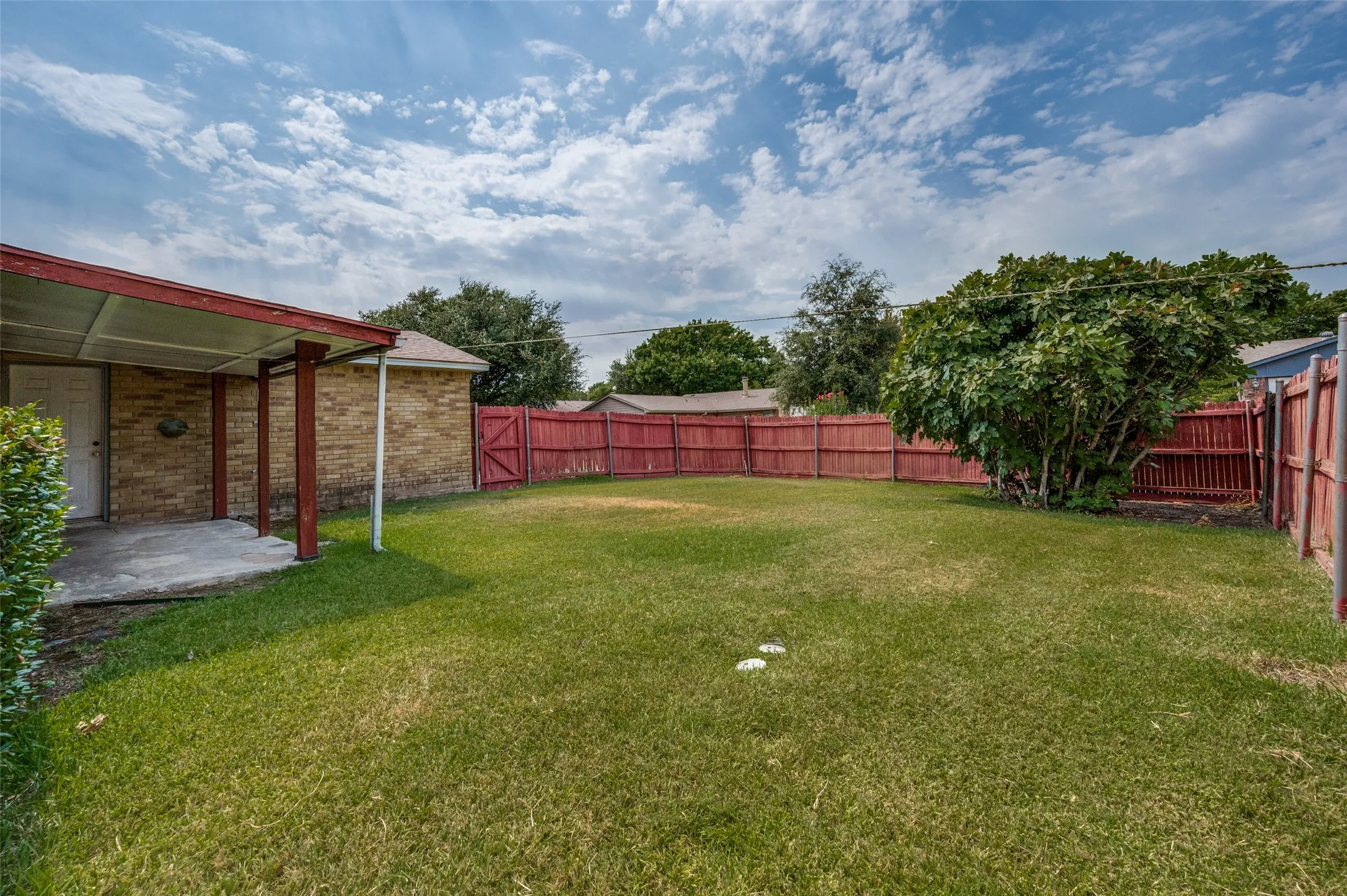 Expansive green lawn, red-stained privacy fencing, mature trees, and a covered concrete patio