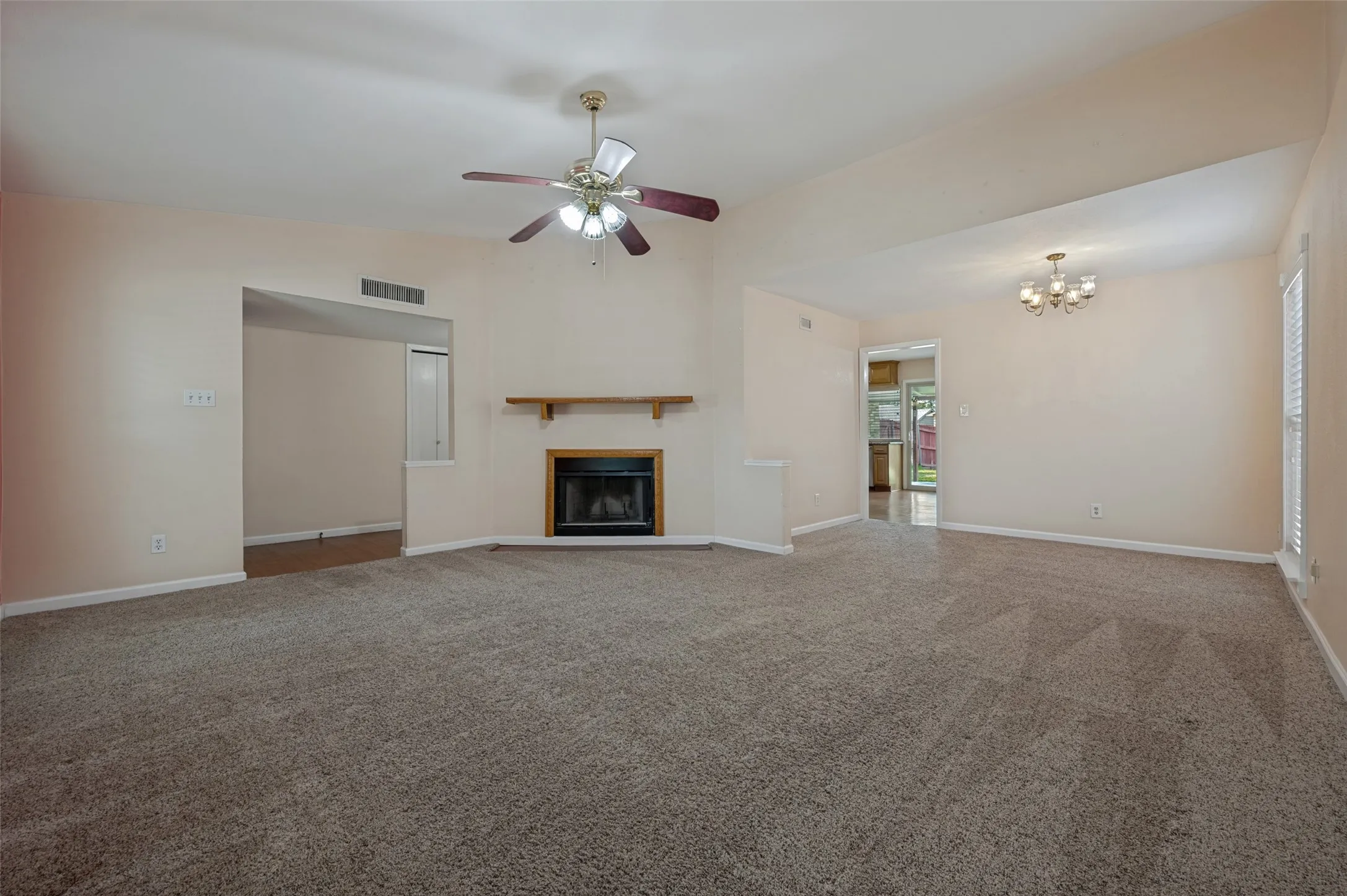 Spacious room featuring vaulted ceilings, a ceiling fan, fireplace with wood mantel, and carpet flooring