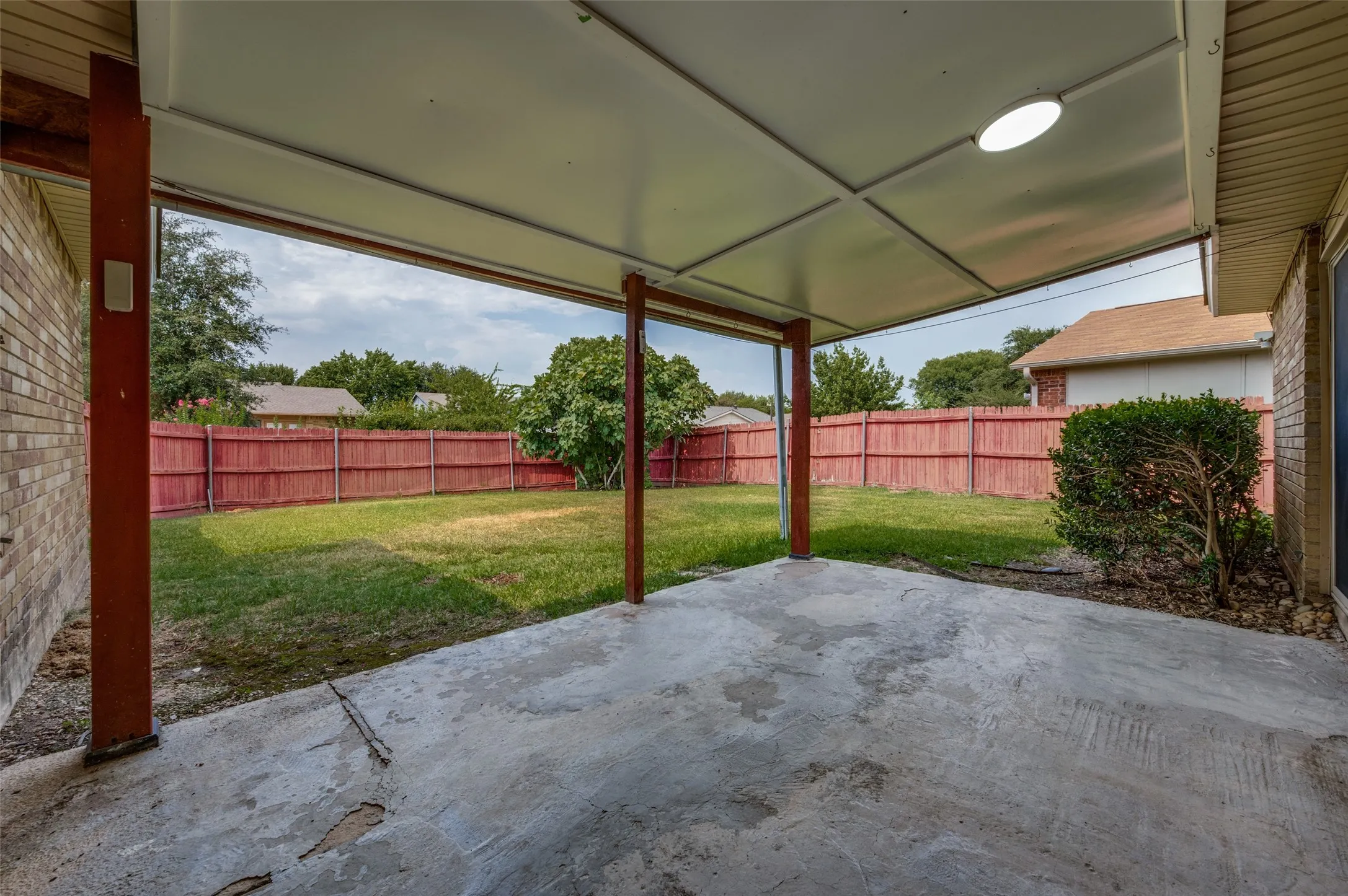 Covered concrete patio with a flat panel ceiling, flush-mount lighting, and brick exterior siding