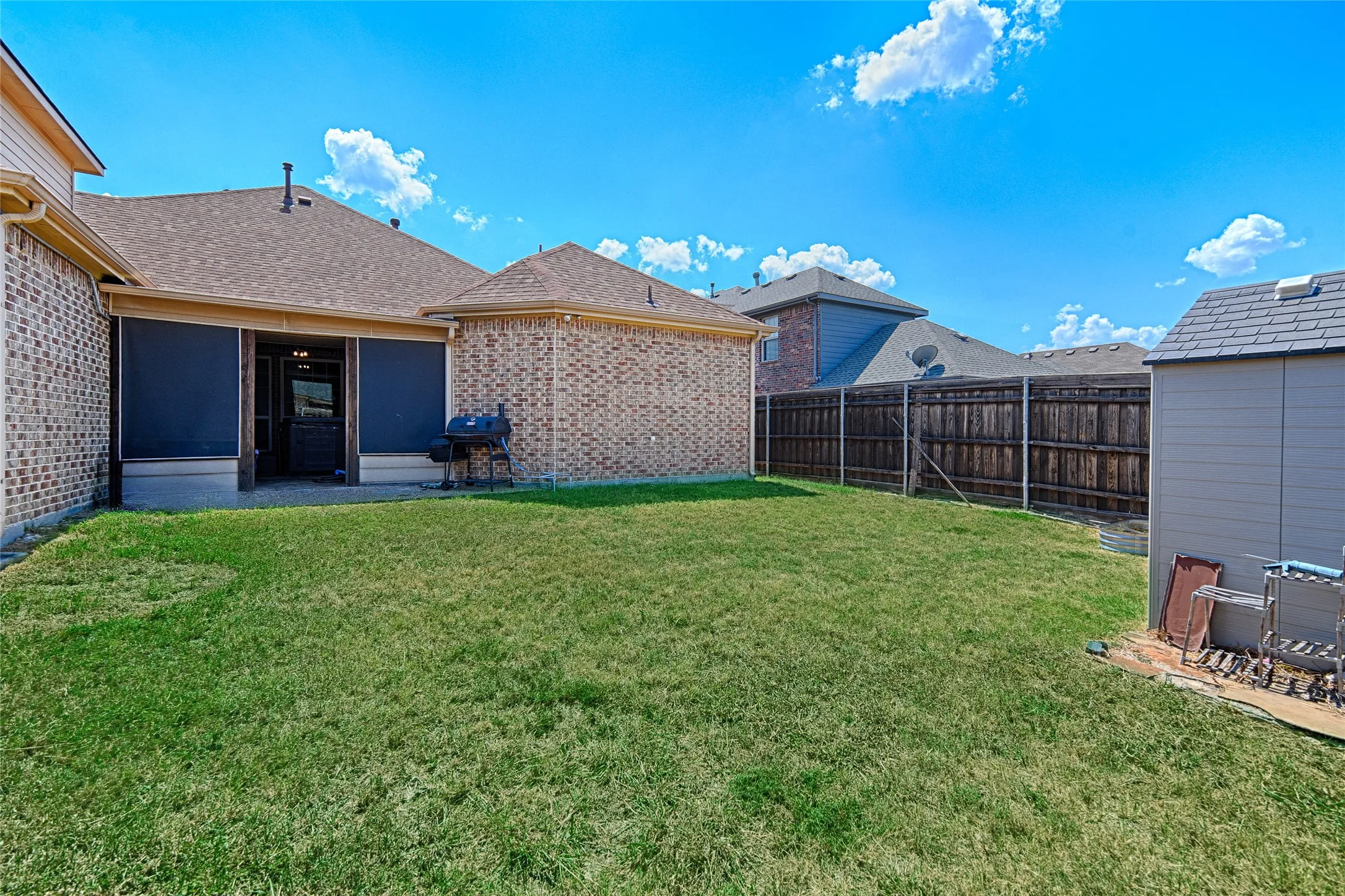 Expansive backyard with a manicured lawn, brick exterior, and a covered patio featuring privacy screens