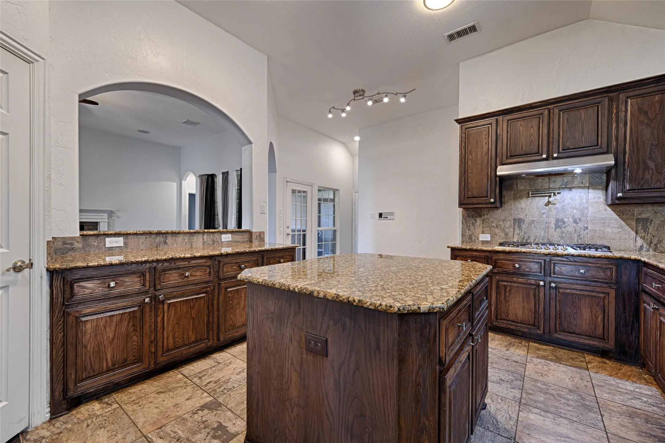 Spacious kitchen featuring an island, dark wood-finish cabinetry, stone countertops, a tile backsplash, and a built-in gas range
