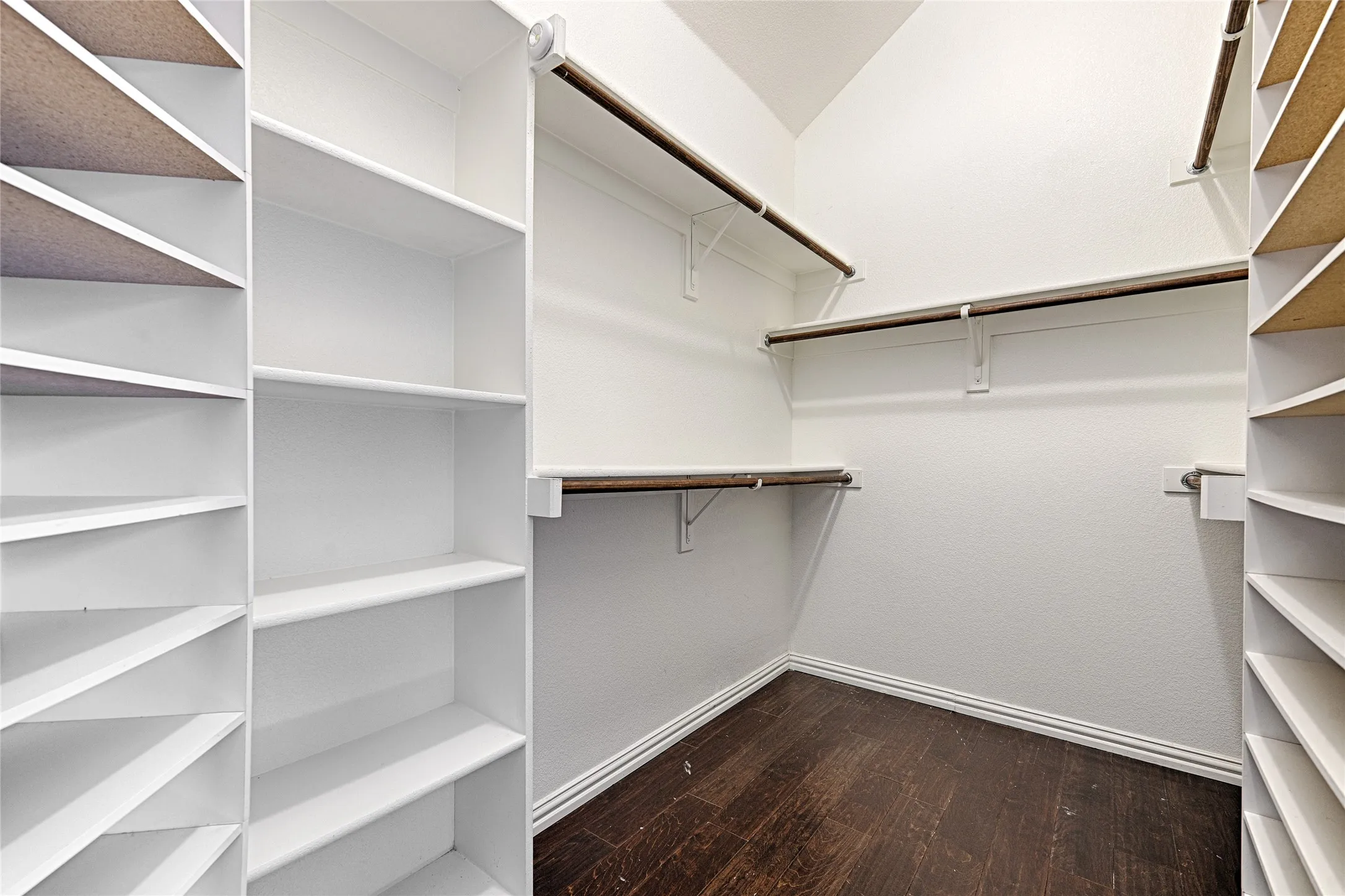 Walk-in closet featuring wood-finish flooring, white walls, multiple hanging rods, and built-in shelving