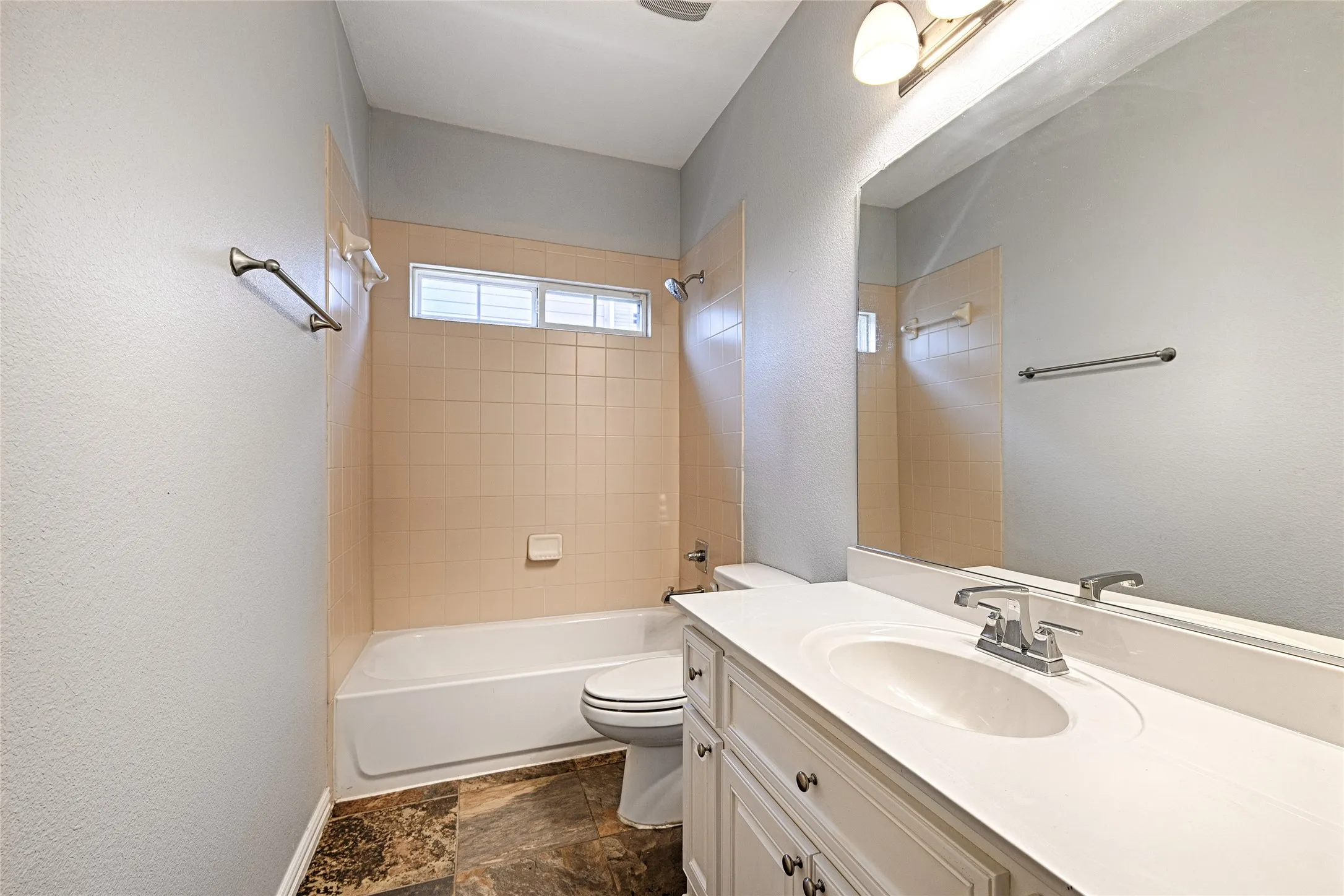 Full bathroom featuring a single vanity with an integrated sink, a large wall-mounted mirror, a tub/shower combination with tiled surround, and patterned floor tiling