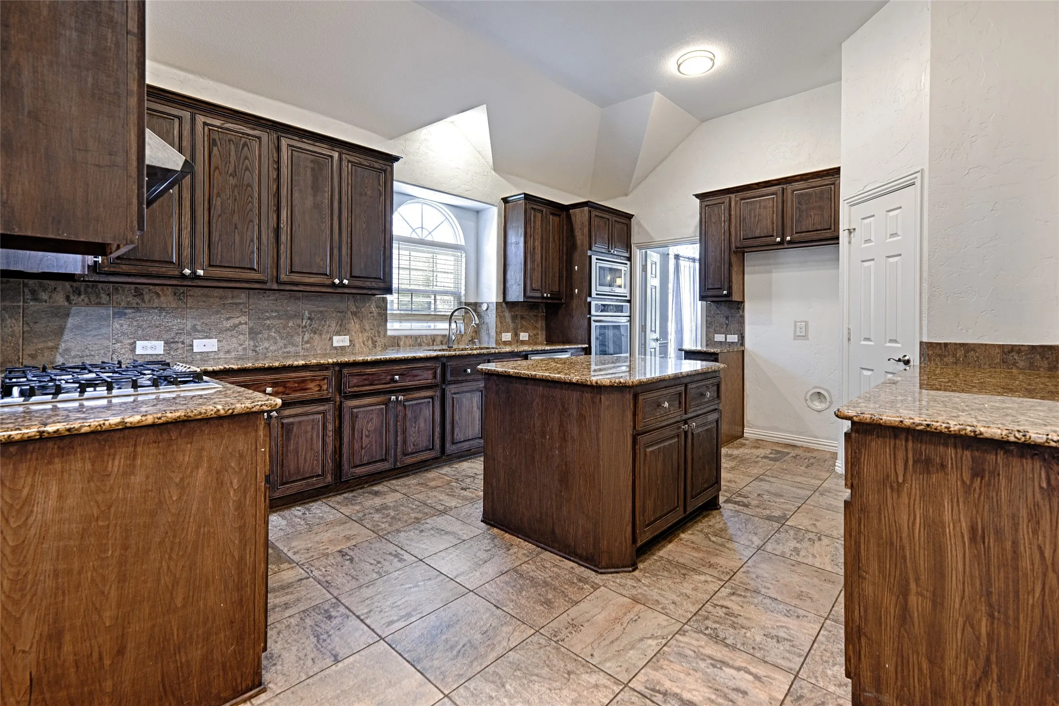 Kitchen featuring wood cabinetry, stone countertops, a gas cooktop, double ovens, and a center island