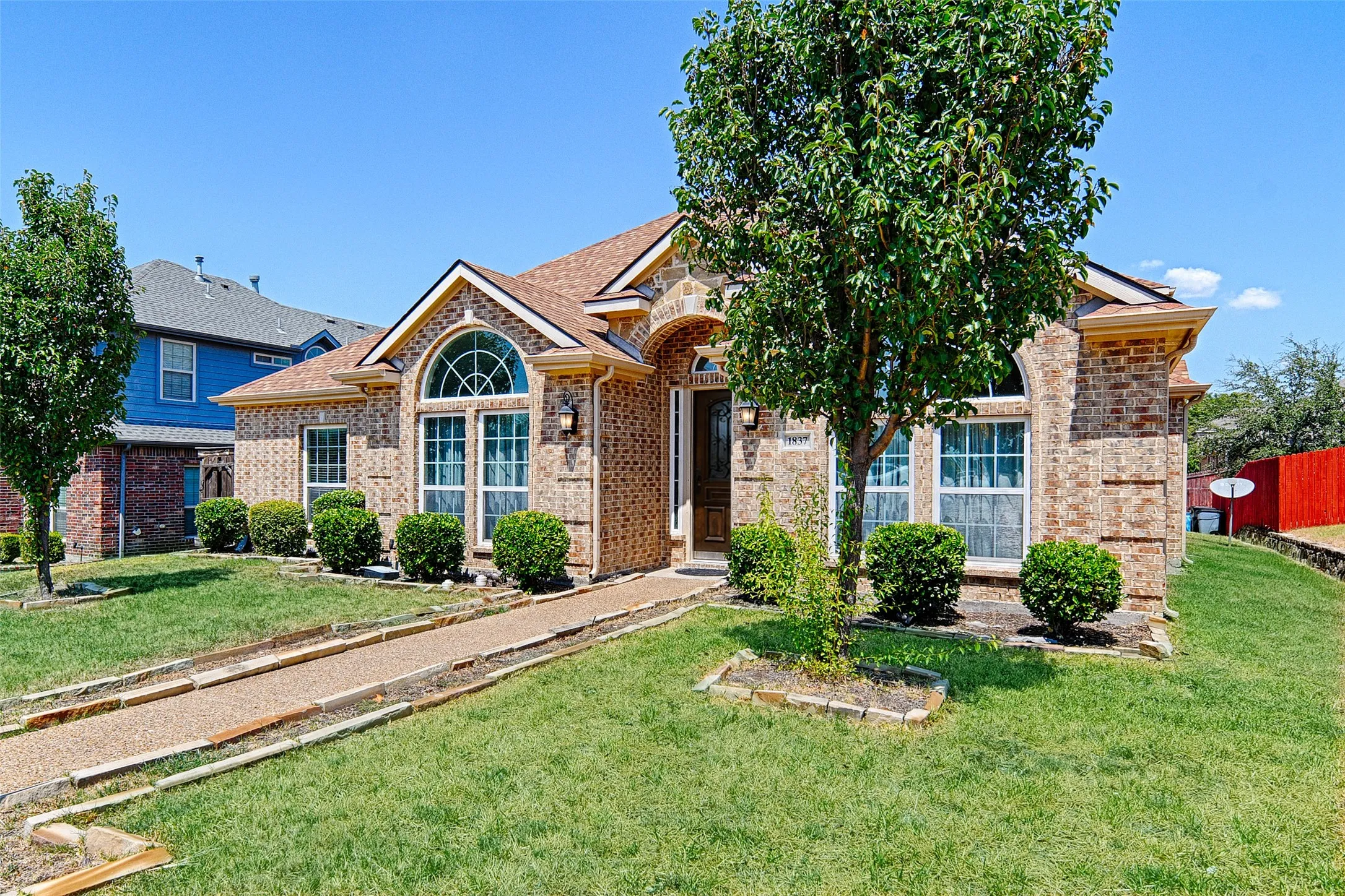 Brick exterior with arched windows, mature landscaping, and a defined walkway leading to the entry