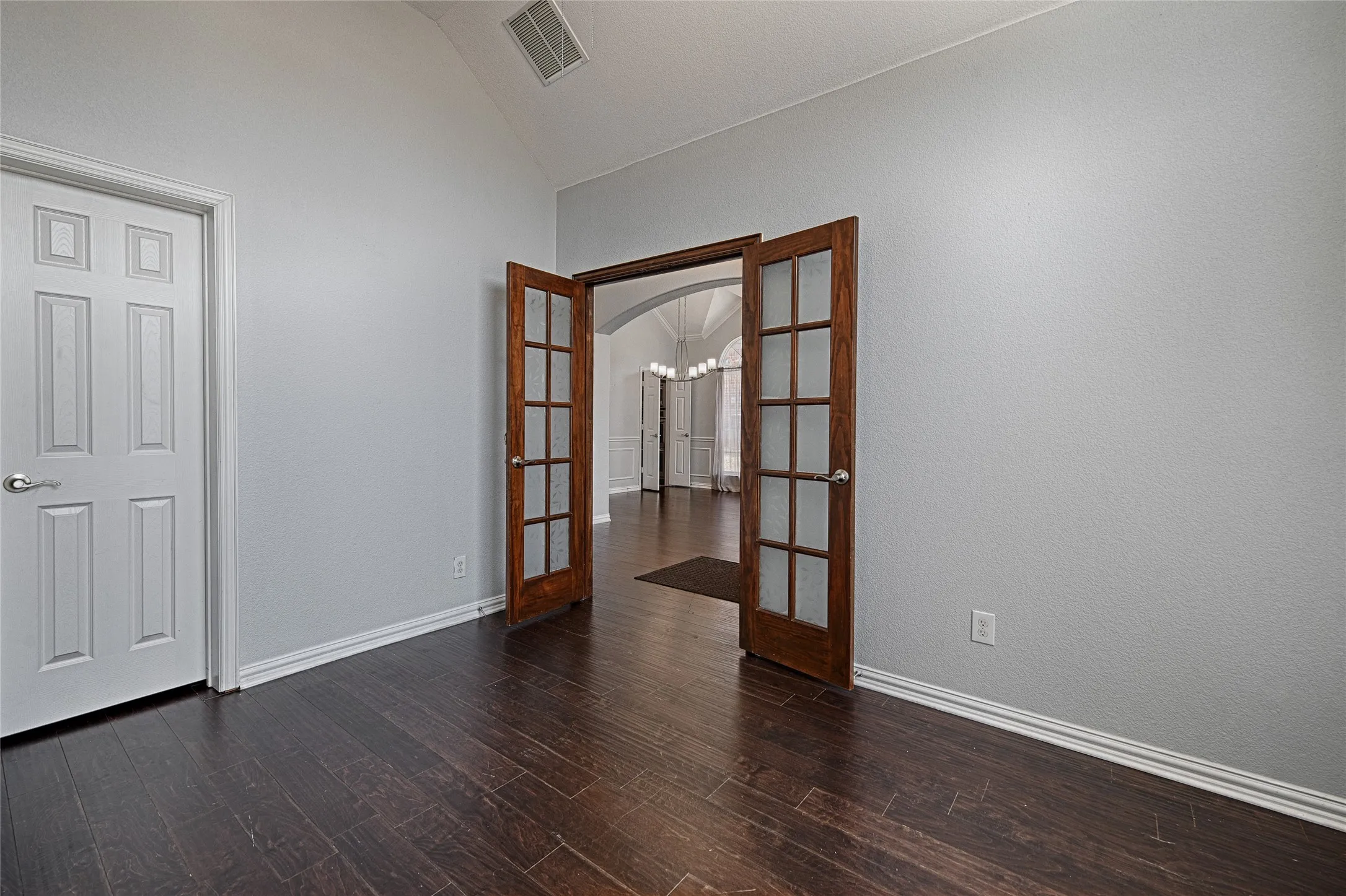 Vaulted ceiling, wood-finish flooring, French doors with glass panels, arched entry, and white paneled door