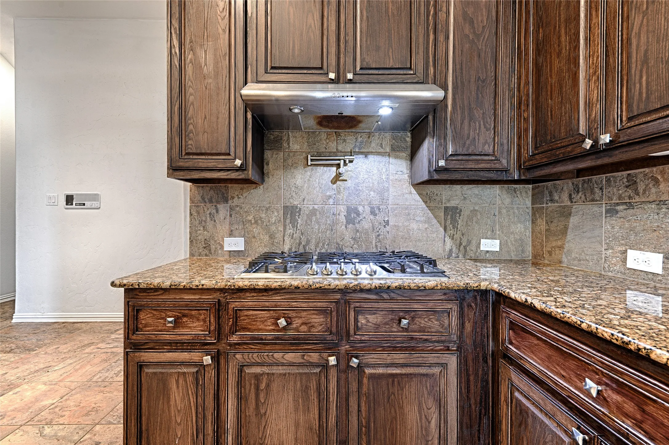 Built-in gas range, pot filler, rich wood cabinetry, granite countertops, and tile backsplash