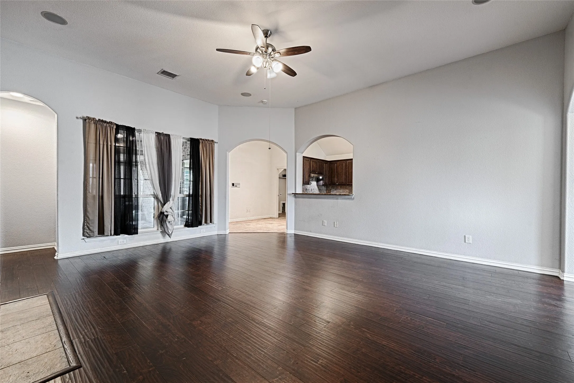 Wood-finish flooring throughout, featuring a vaulted ceiling with a ceiling fan, recessed lighting, and arched doorways