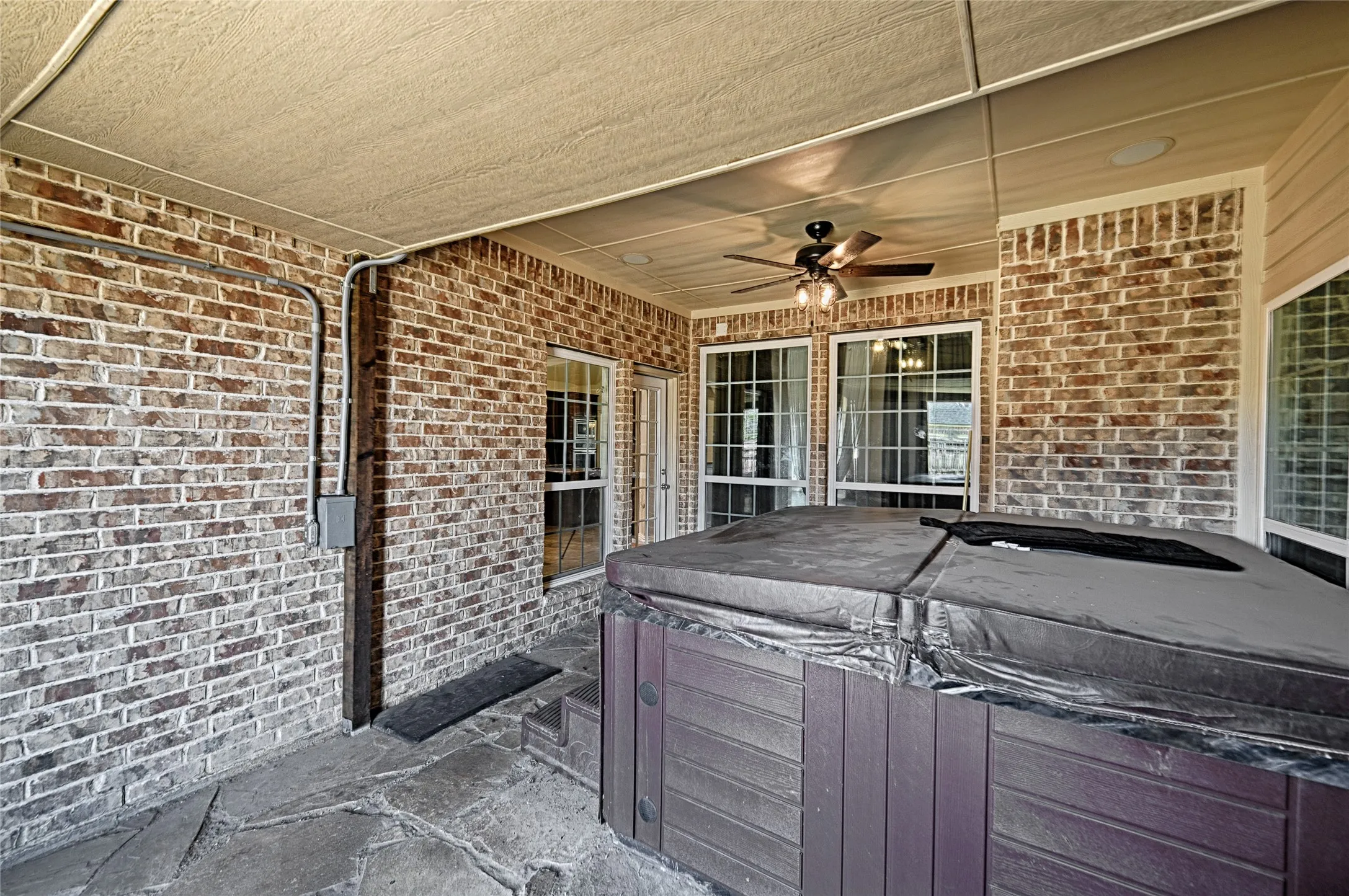 Covered patio with flagstone flooring, brick wall finishes, and a ceiling fan