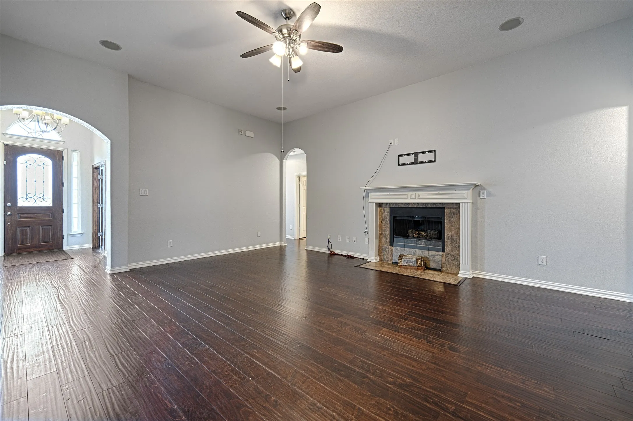 Hardwood flooring, arched doorways, fireplace with stone surround and mantle, and a ceiling fan with integrated lighting